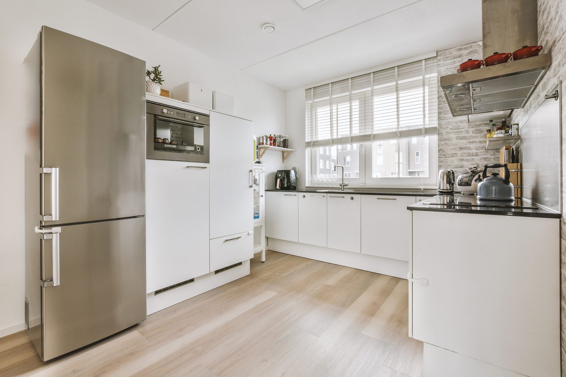 A modern kitchen with white cabinets, stainless steel appliances, wood floor, and a window.