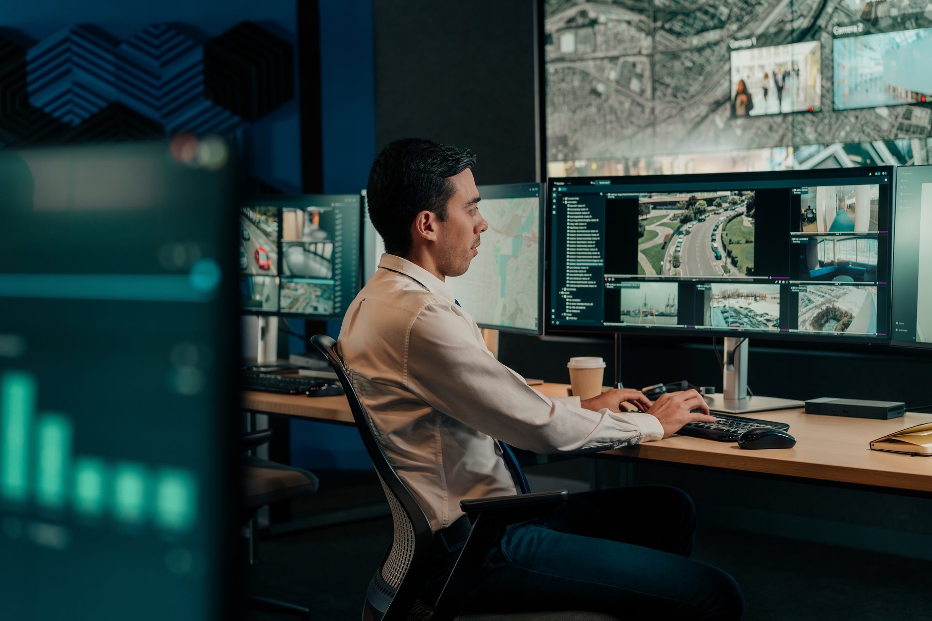Man in a control room monitors security footage and maps on multiple screens.