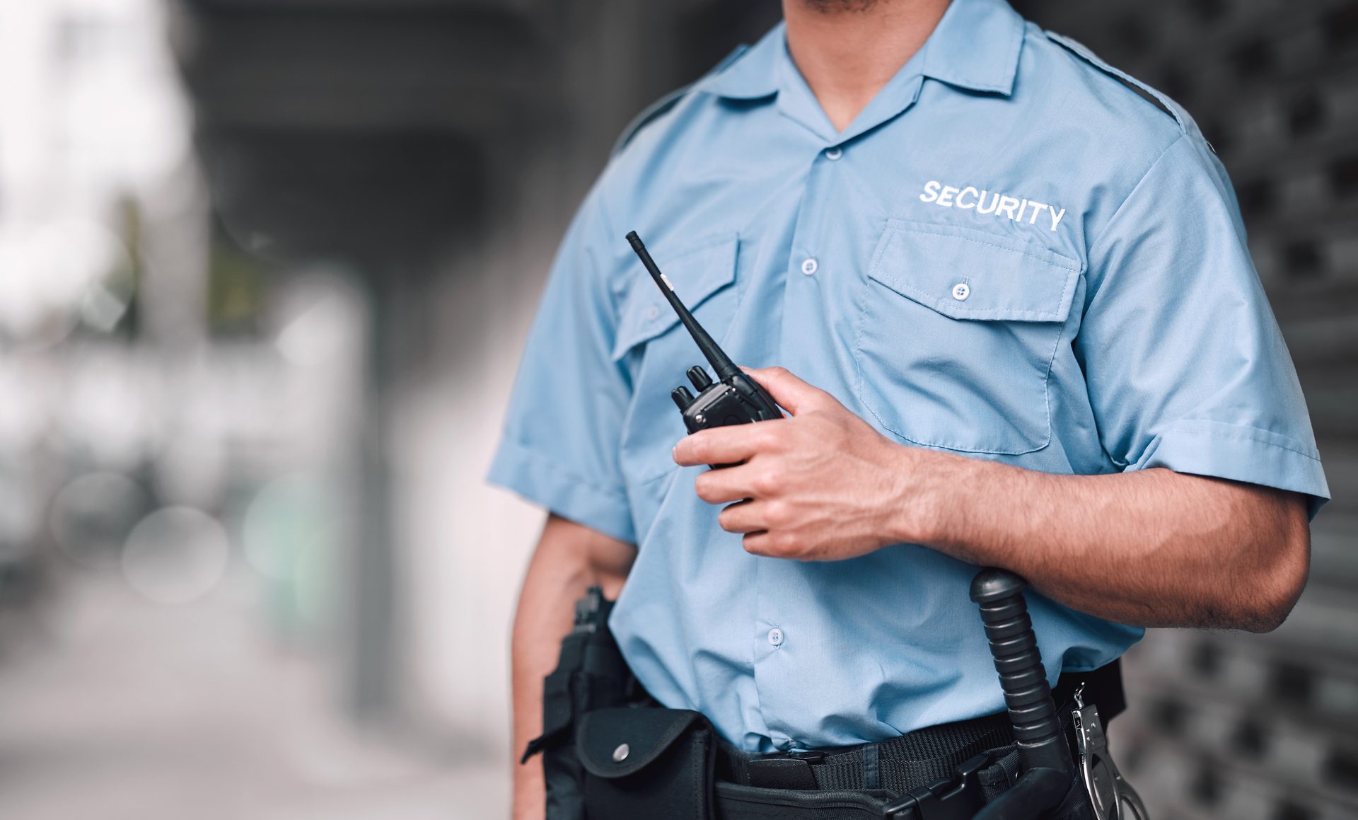 A security guard in a light blue uniform holds a walkie-talkie. The word "SECURITY" is visible on the shirt.