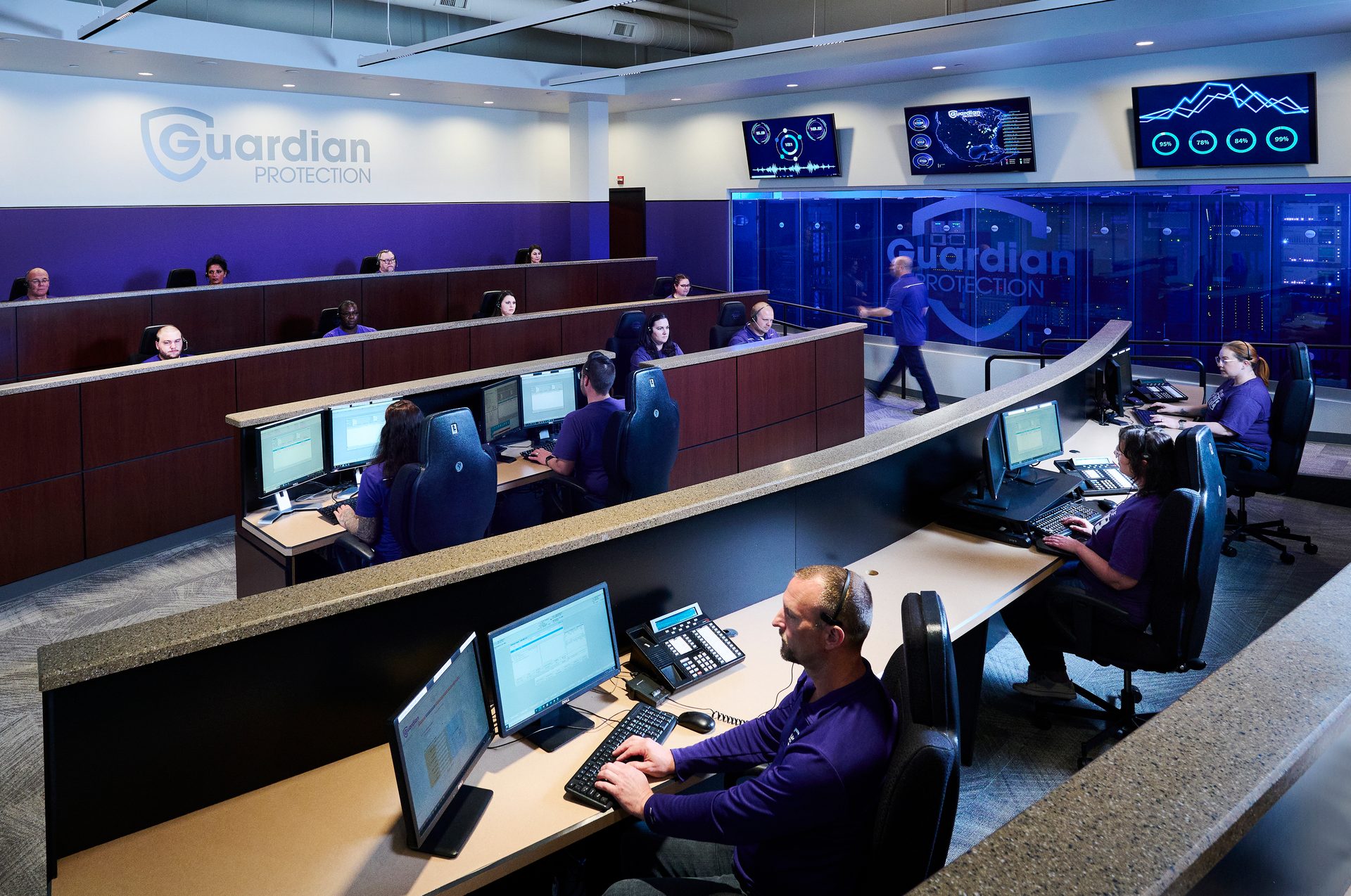 Guardian Protection operations center with numerous agents working at computers and large data screens.