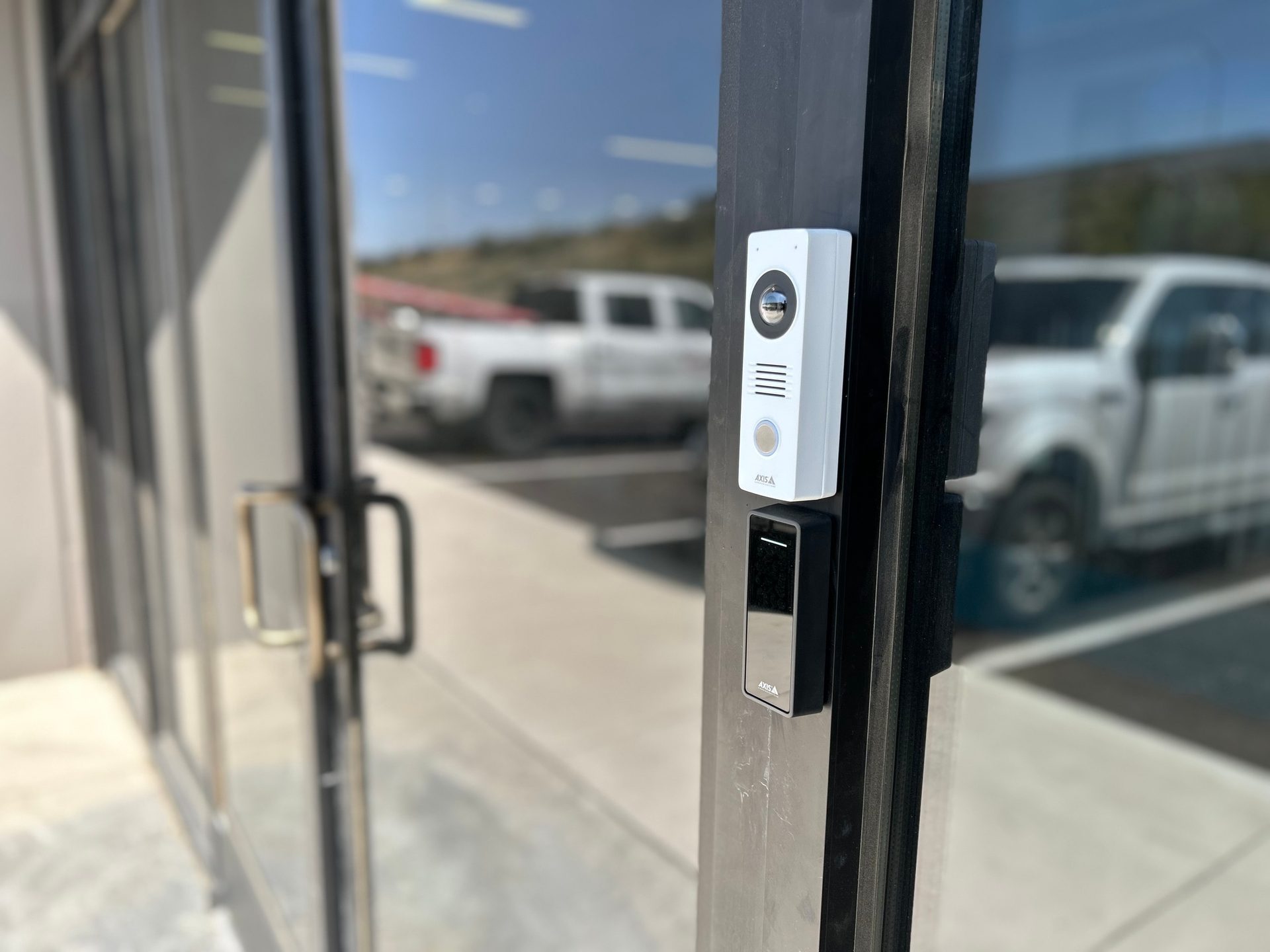 Axis A video intercom and card reader on a glass door, with a white truck reflected outside.