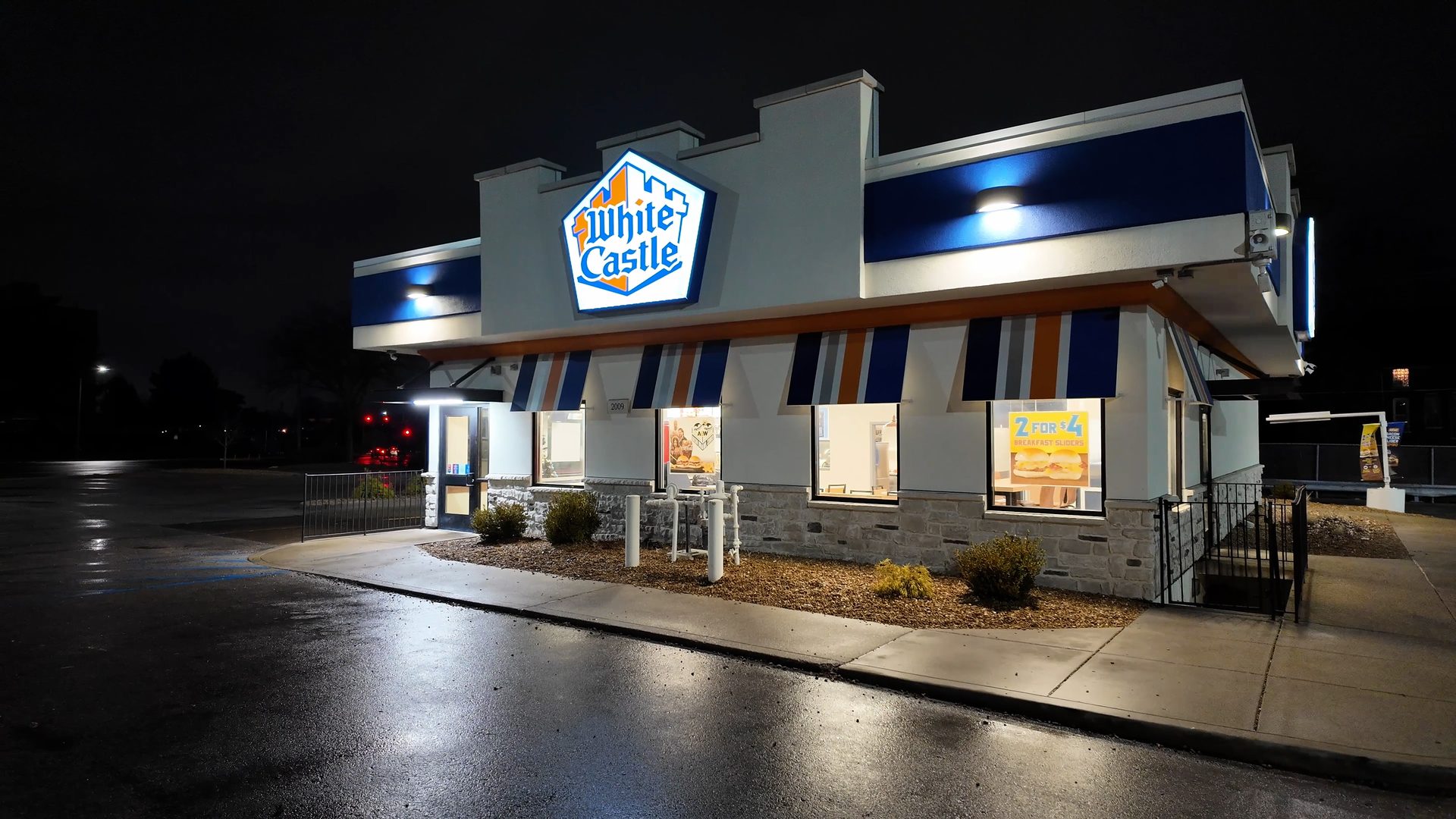 Exterior of a White Castle restaurant at night, illuminated, with a wet parking lot.