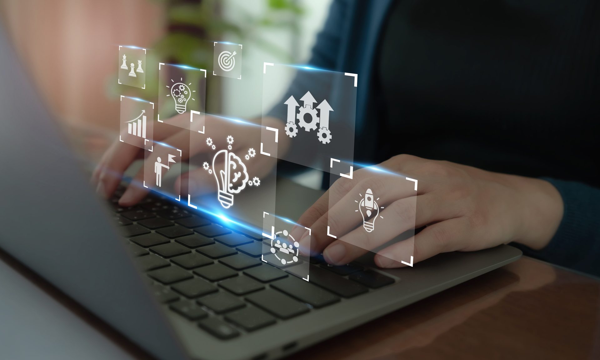 Hands on laptop with glowing holographic business icons: ideas, strategy, growth.