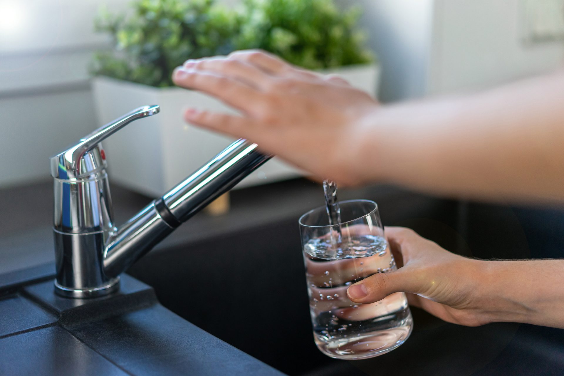 Hand filling a glass of water from a faucet.