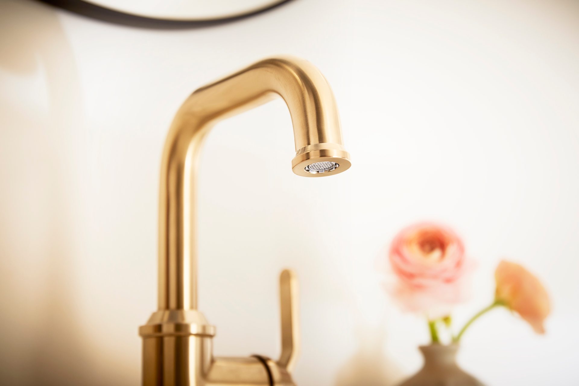 Brushed gold faucet with blurred pink flowers in the background.