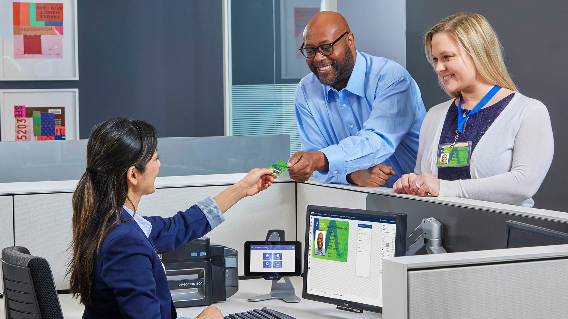An employee hands a new ID card to a smiling male colleague, while another female colleague watches.