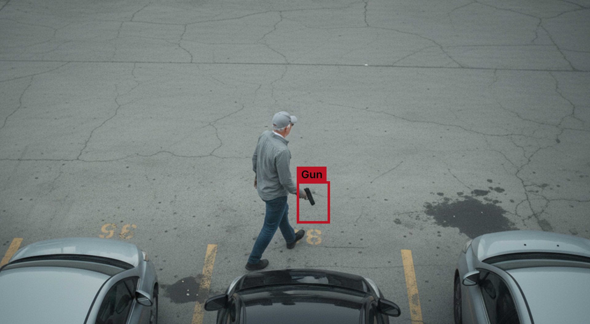An overhead shot of a man walking in a parking lot, holding a black handgun.