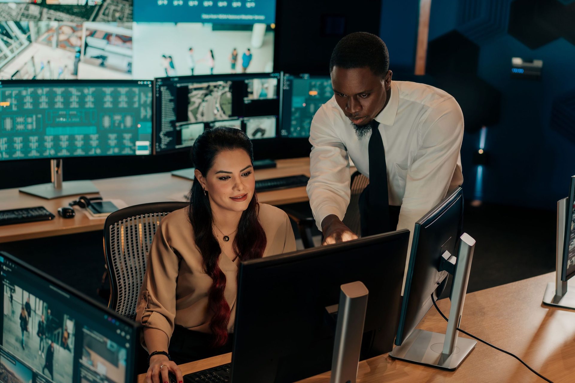 Two security analysts collaborating in a control room with multiple monitors.