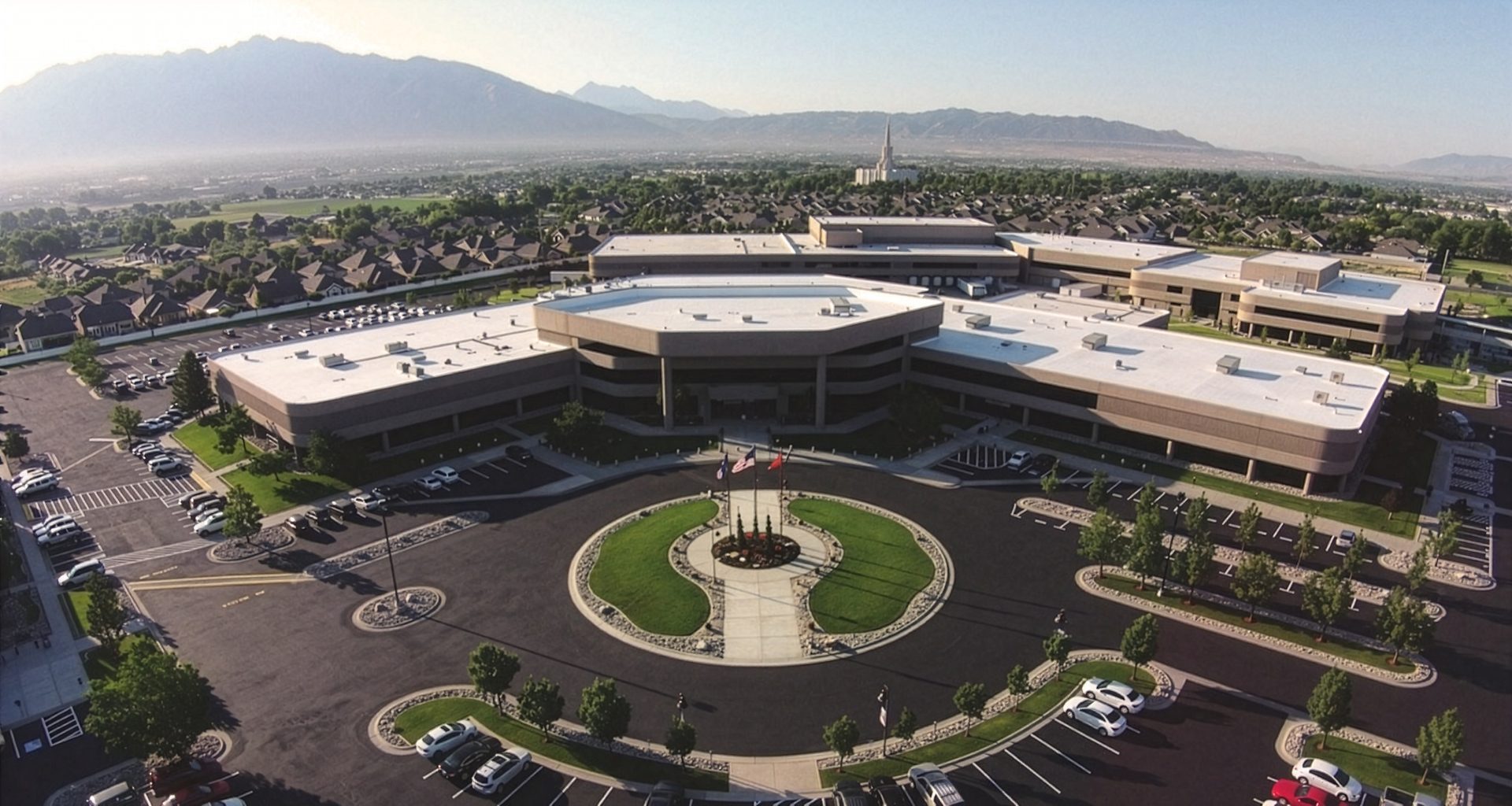 Aerial view of a large corporate campus with a circular drive, parking lots, mountains, and a temple spire.
