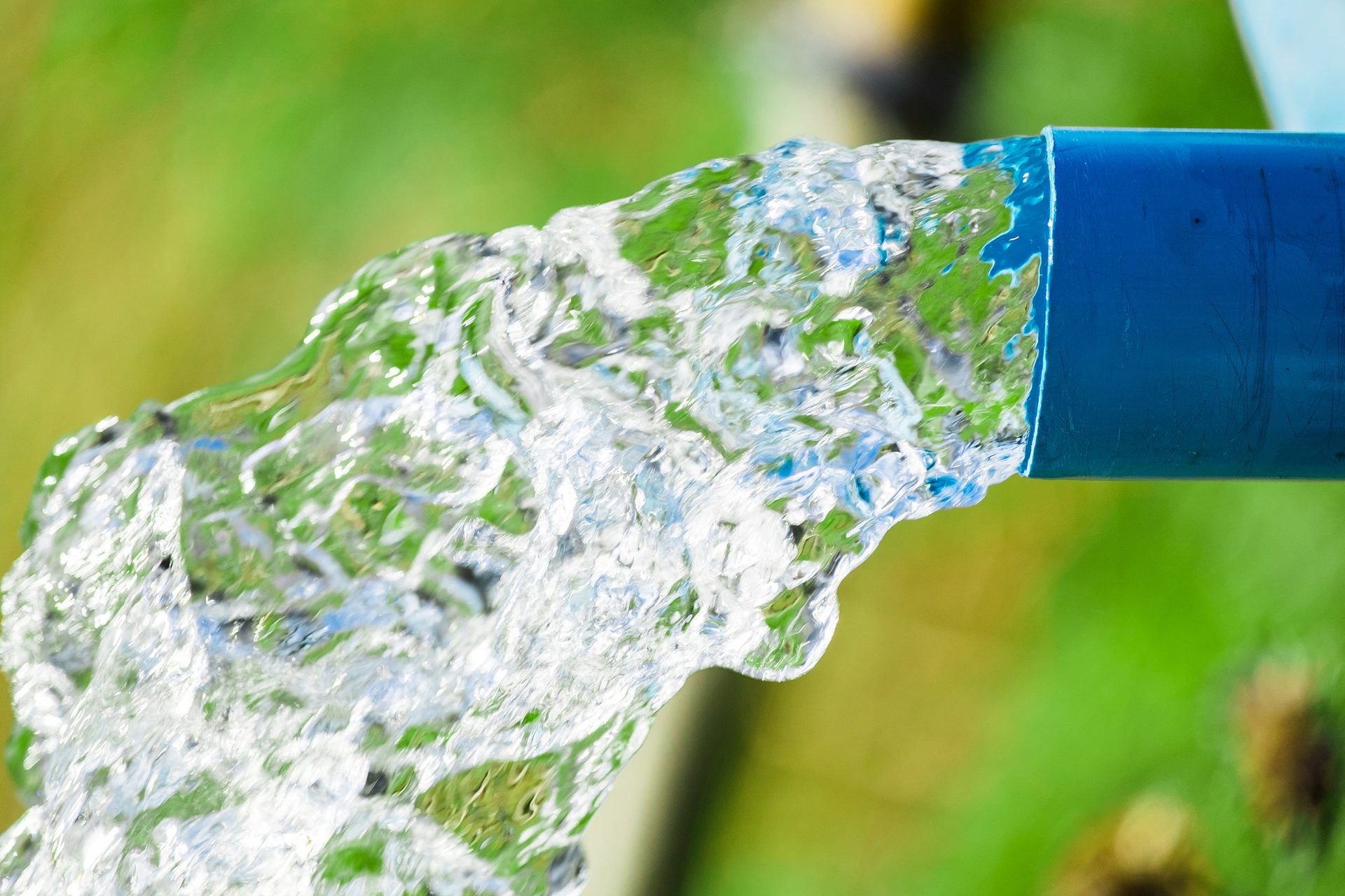 Clear water gushing from a blue pipe with a blurry green background.