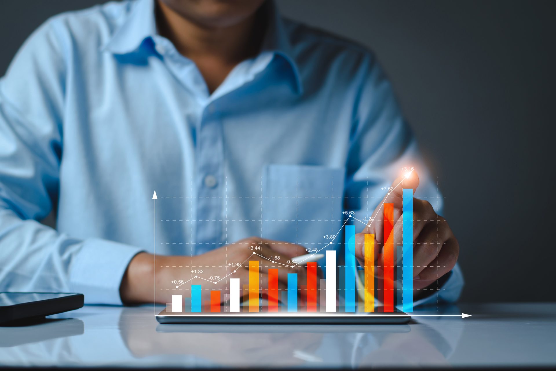 A person in a blue shirt interacts with a holographic bar chart showing growth on a digital tablet.