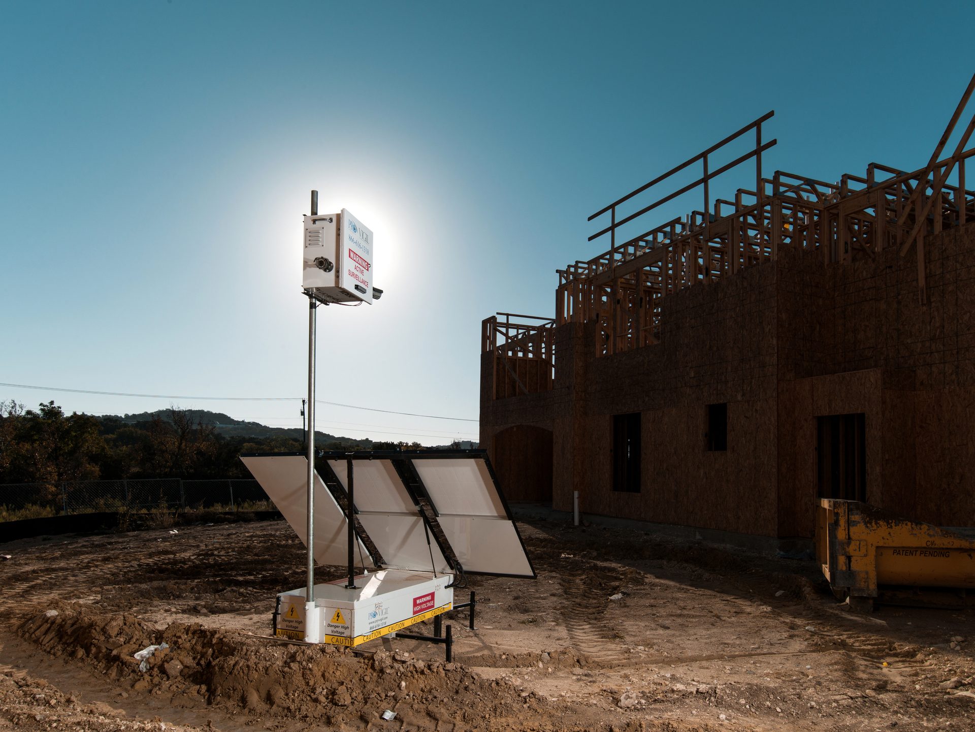 A ProVigil security camera with solar panels overlooks a dirt construction site with an unfinished house.