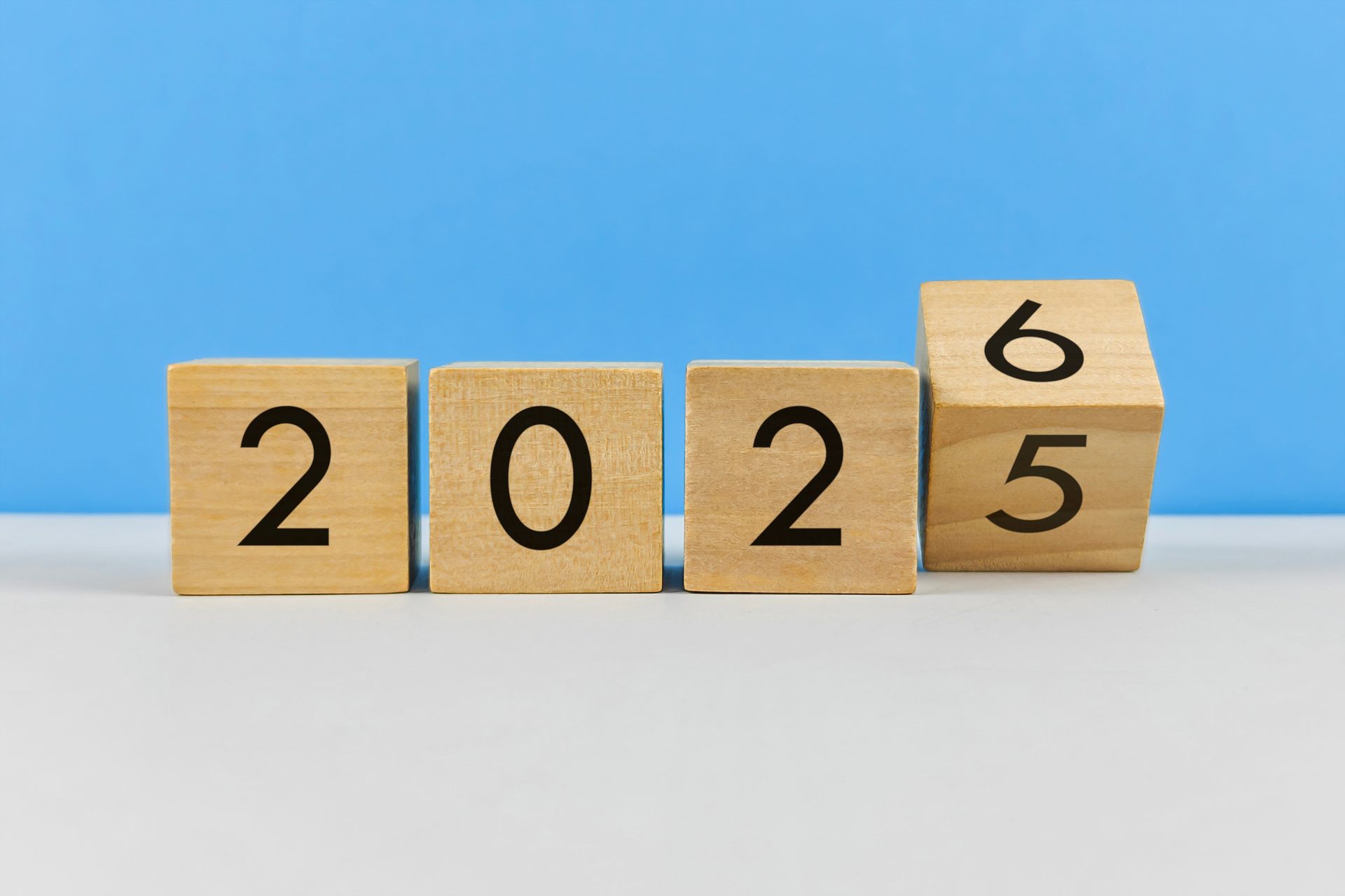 Wooden blocks spell "2025". The last block is rotated, showing "6" above "5", hinting at 2026.