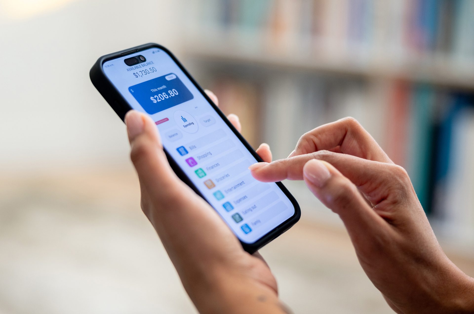 Close-up of hands using a smartphone with a financial app displaying spending and balance.