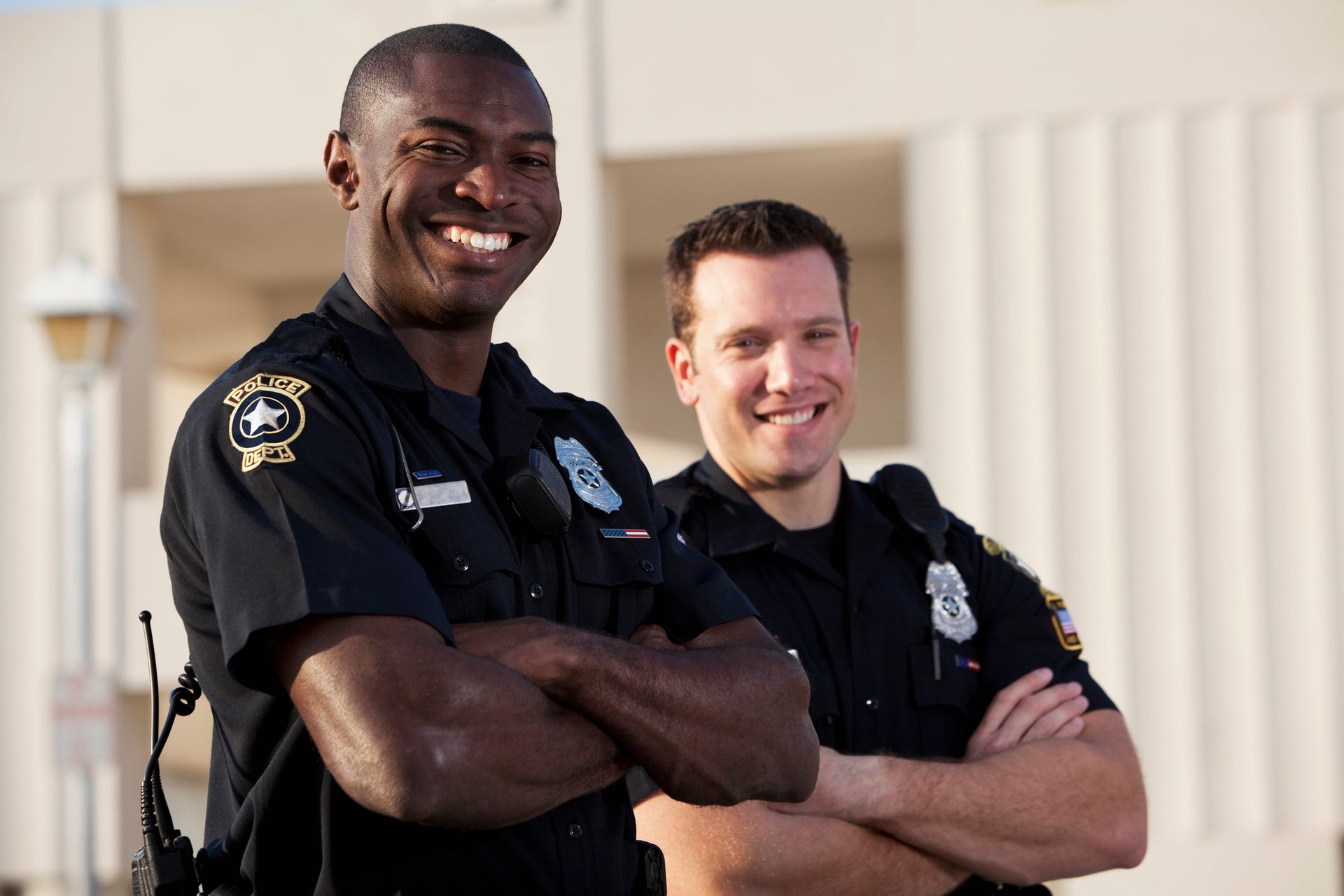 Smiling Black and White male police officers, arms crossed.