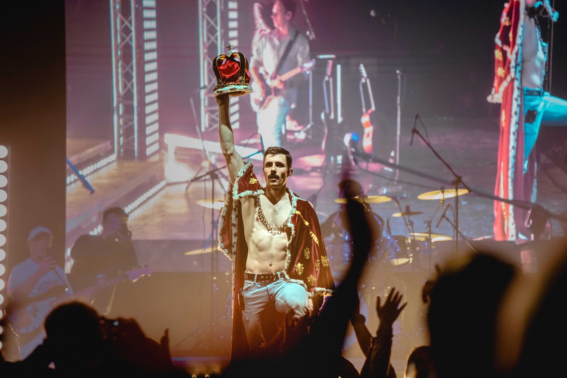 Freddie Mercury impersonator holds crown aloft on stage at a concert.