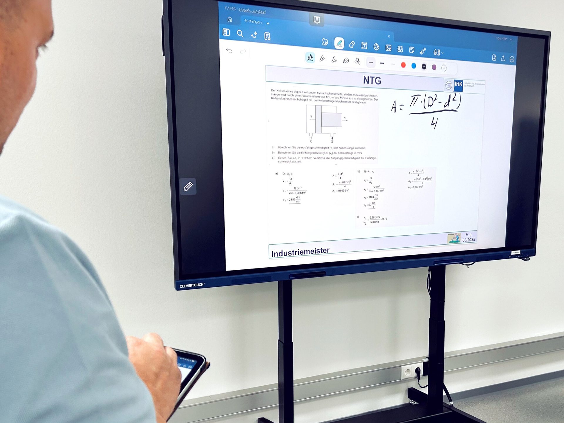 Man uses a tablet to interact with a large display showing engineering calculations and text for training.