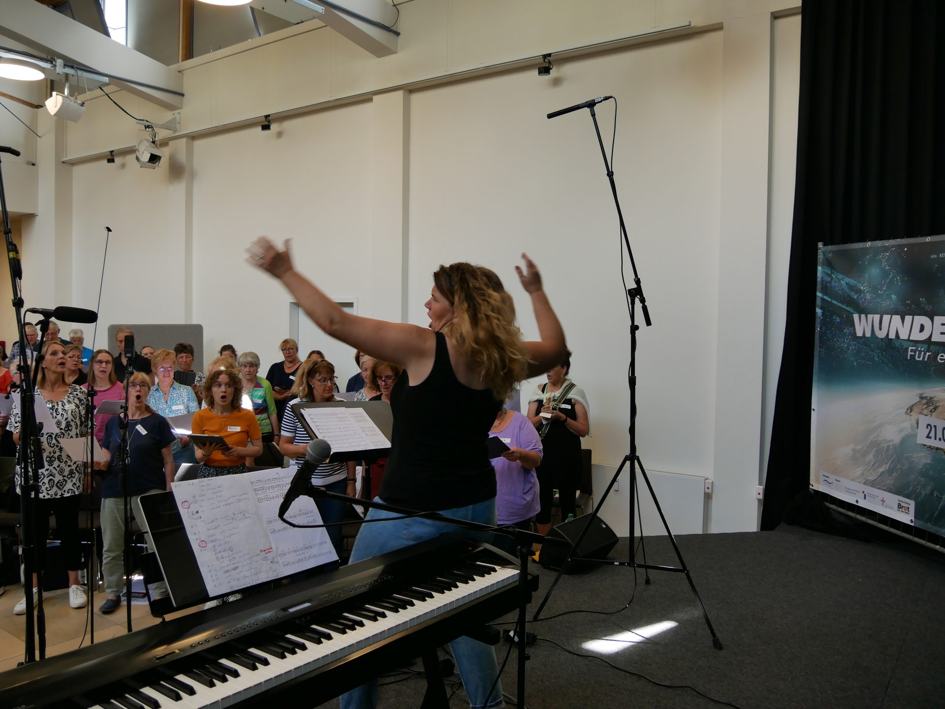 Conductor leading a choir of older women with an electronic keyboard in front.