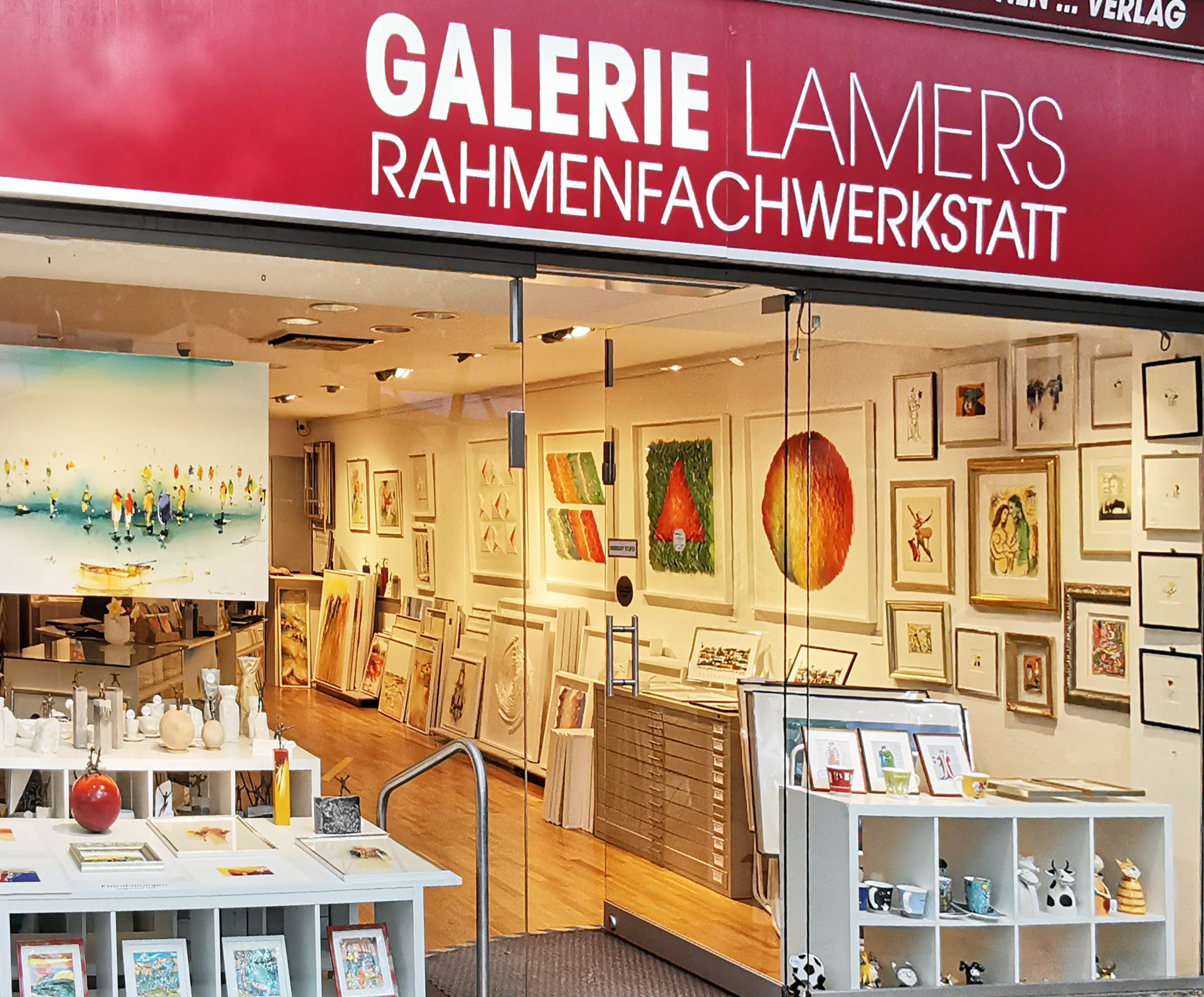 Shopfront of "Galerie Lamers Rahmenfachwerkstatt" displaying many framed artworks and decorative items.