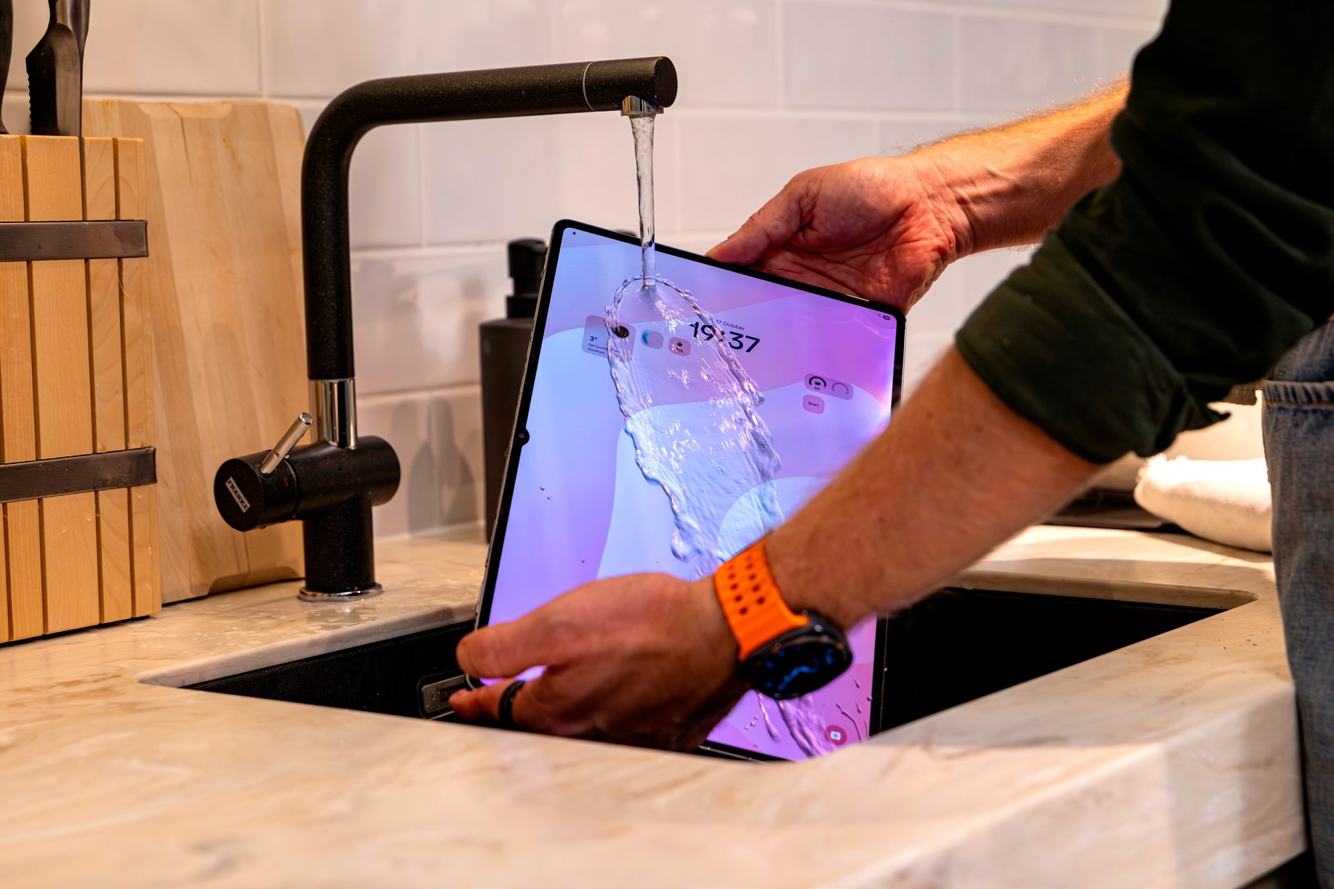 Tablet being rinsed under running water in a kitchen sink.