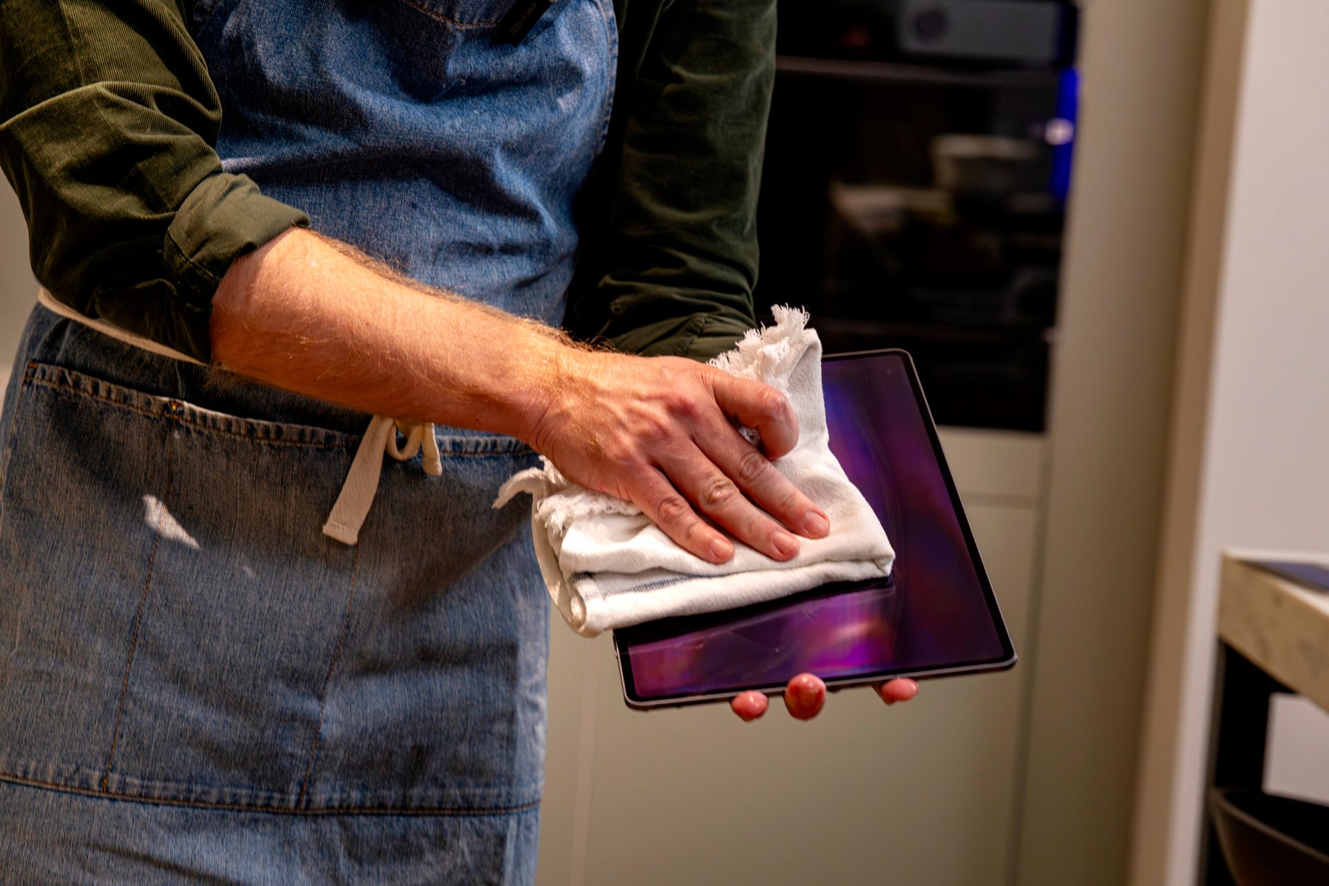 Person in apron wipes a tablet screen with a white cloth.