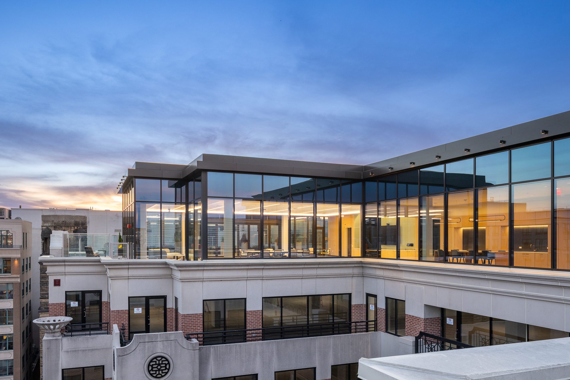 Exterior of a building with a modern glass rooftop lounge on a traditional facade, under twilight.