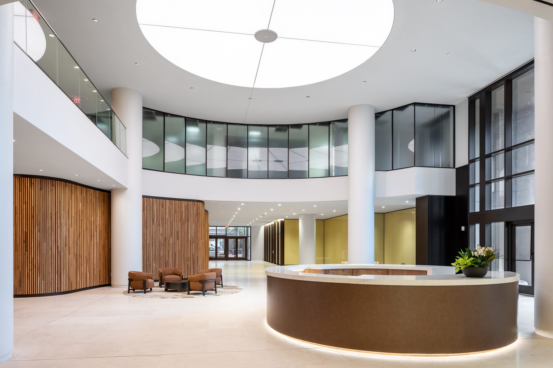 Elegant, bright lobby featuring a curved reception, lounge area, wood walls, and circular ceiling light.