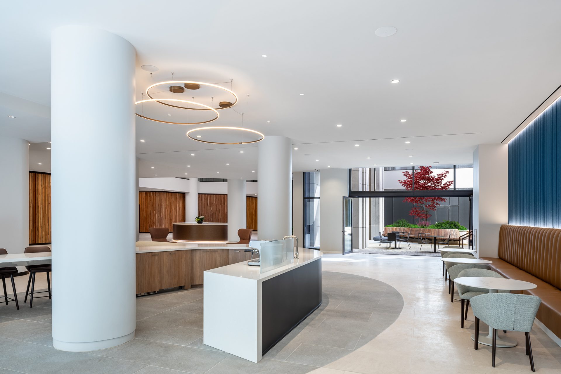 Modern lobby with coffee bar, reception, seating, and outdoor courtyard with a red tree.