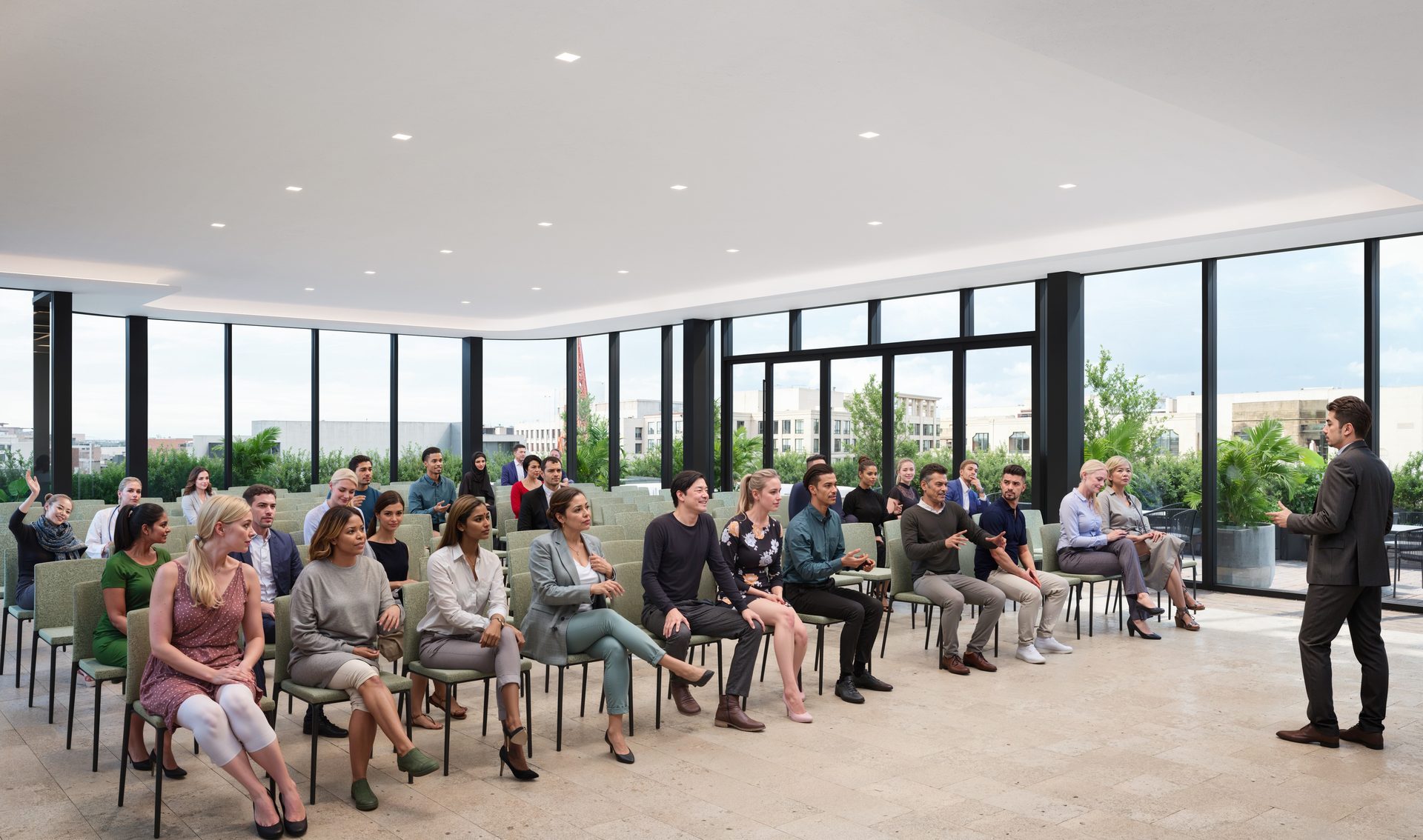 Speaker presenting to an audience in a modern room with large windows.