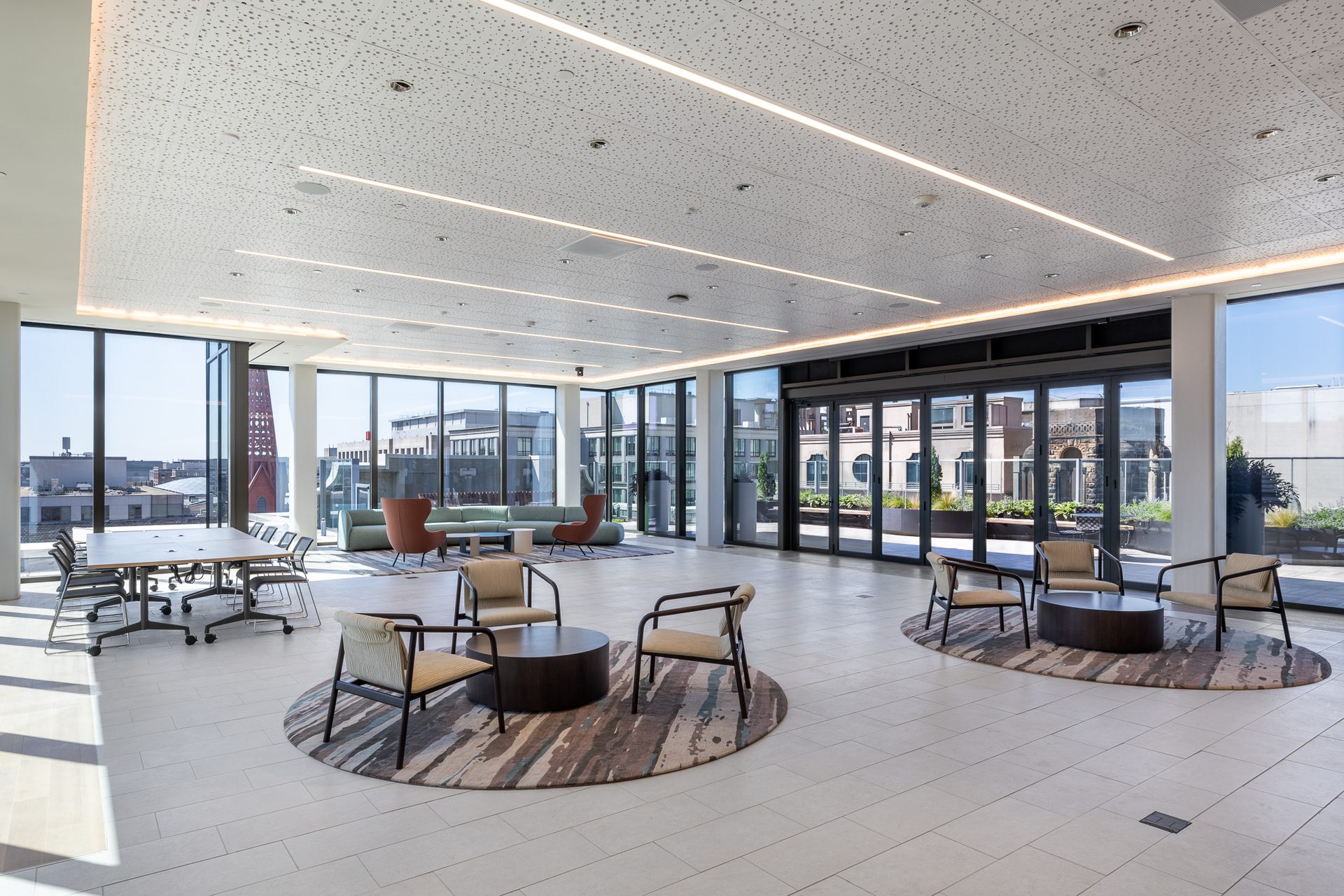 Spacious, modern office lounge with various seating areas, large windows, and a perforated ceiling.