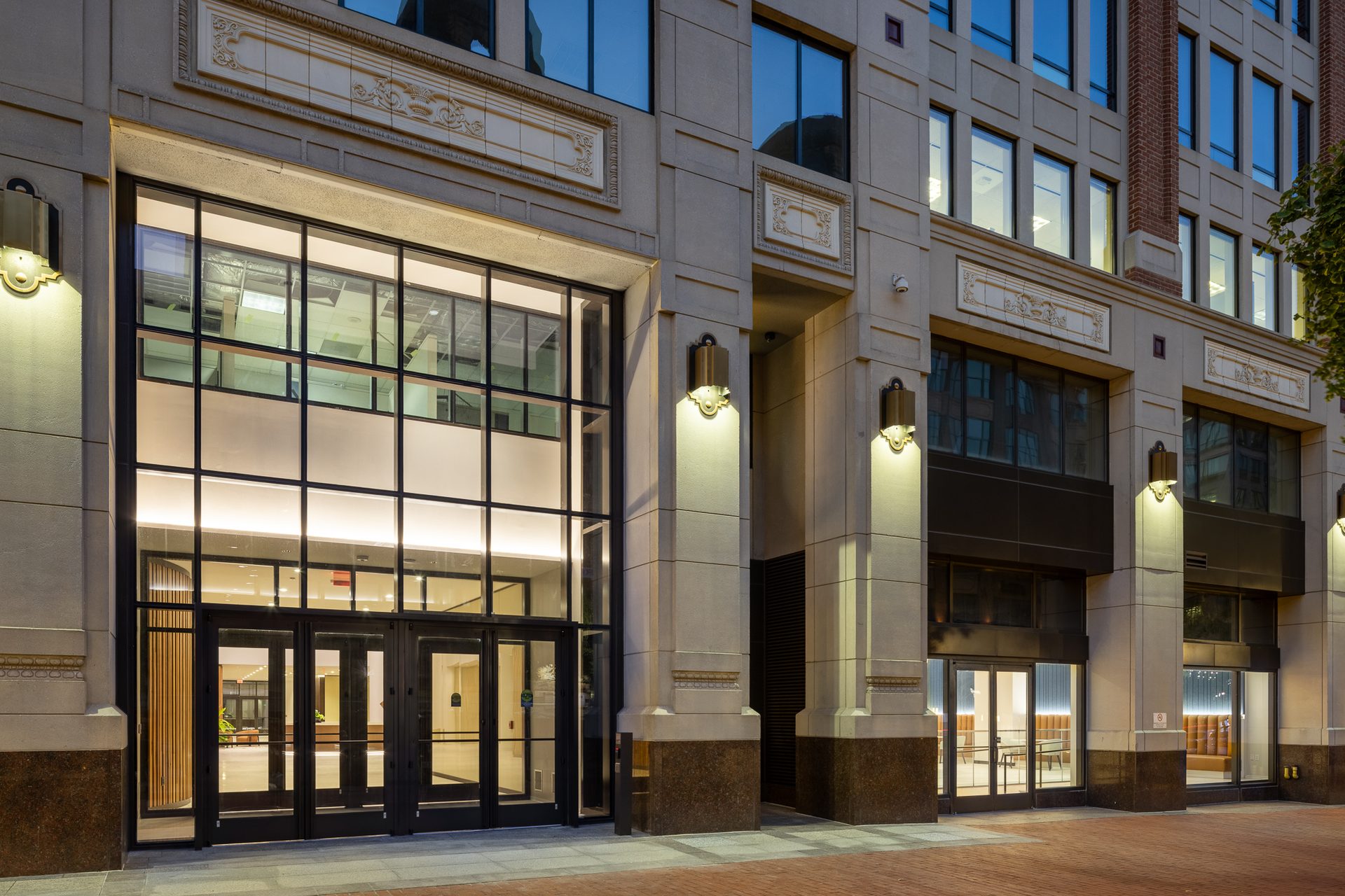 Night view of a modern building facade with large glass entrances, warm interior lighting, and decorative upper details.