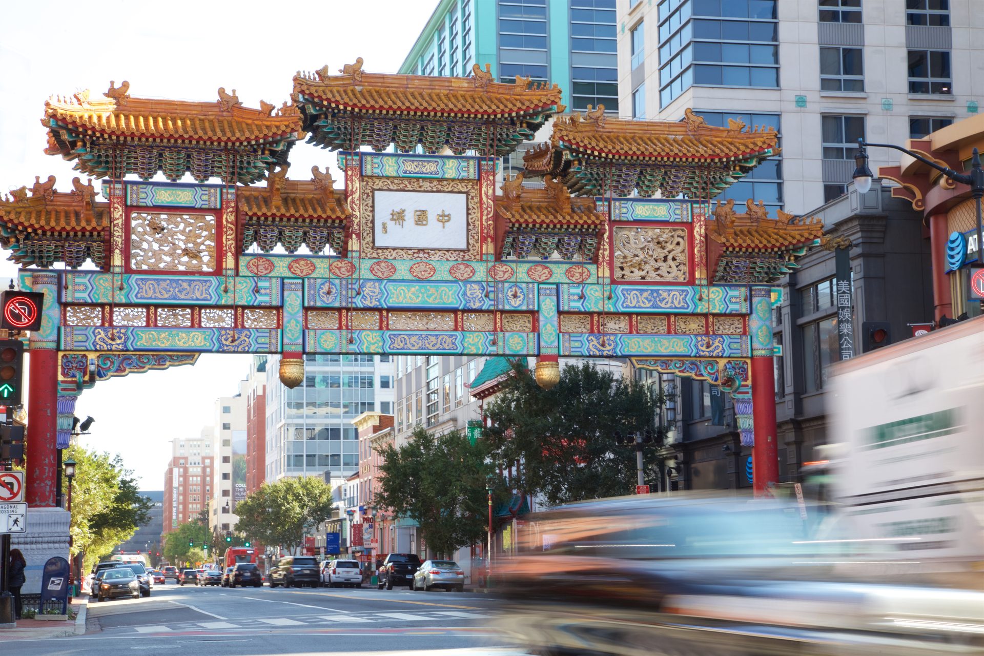 Colorful Chinatown arch over a busy street with blurred cars and buildings in the background.
