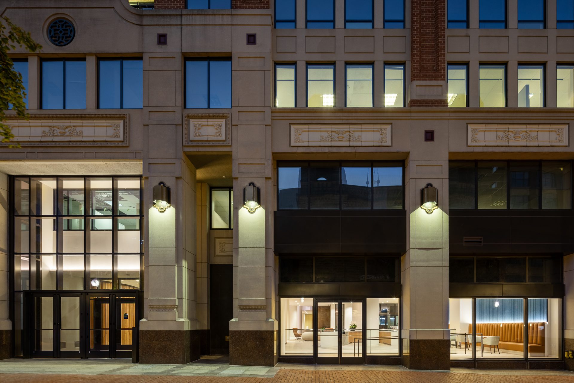Building facade with glowing ground-floor entrances and decorative details at dusk.