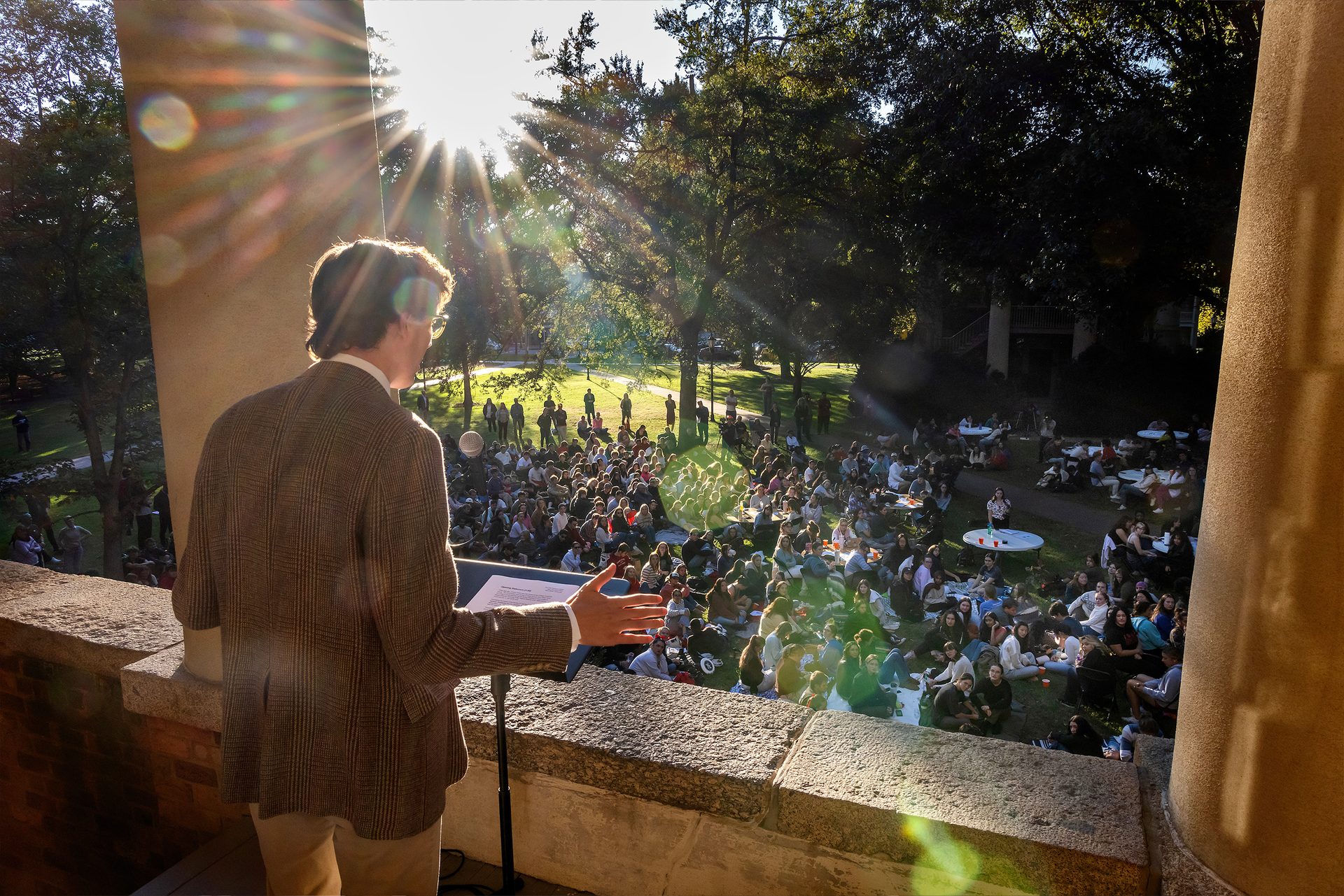 A student with a brown corduroy blazer addresses a crowd of students on the historic green between Philanthropic and Eumanean halls