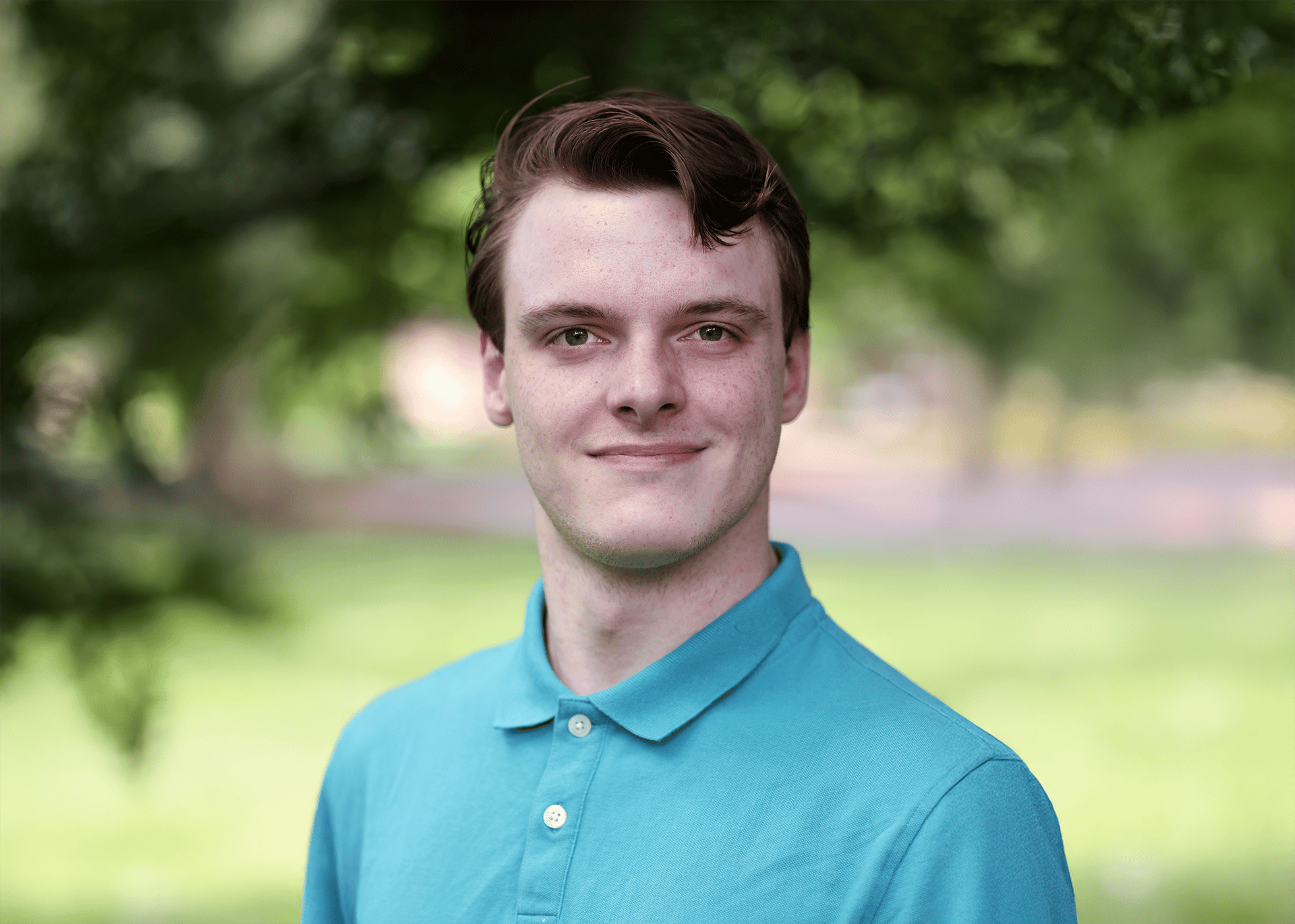 White student with brown hair and an aqua green polo shirt smiles softly