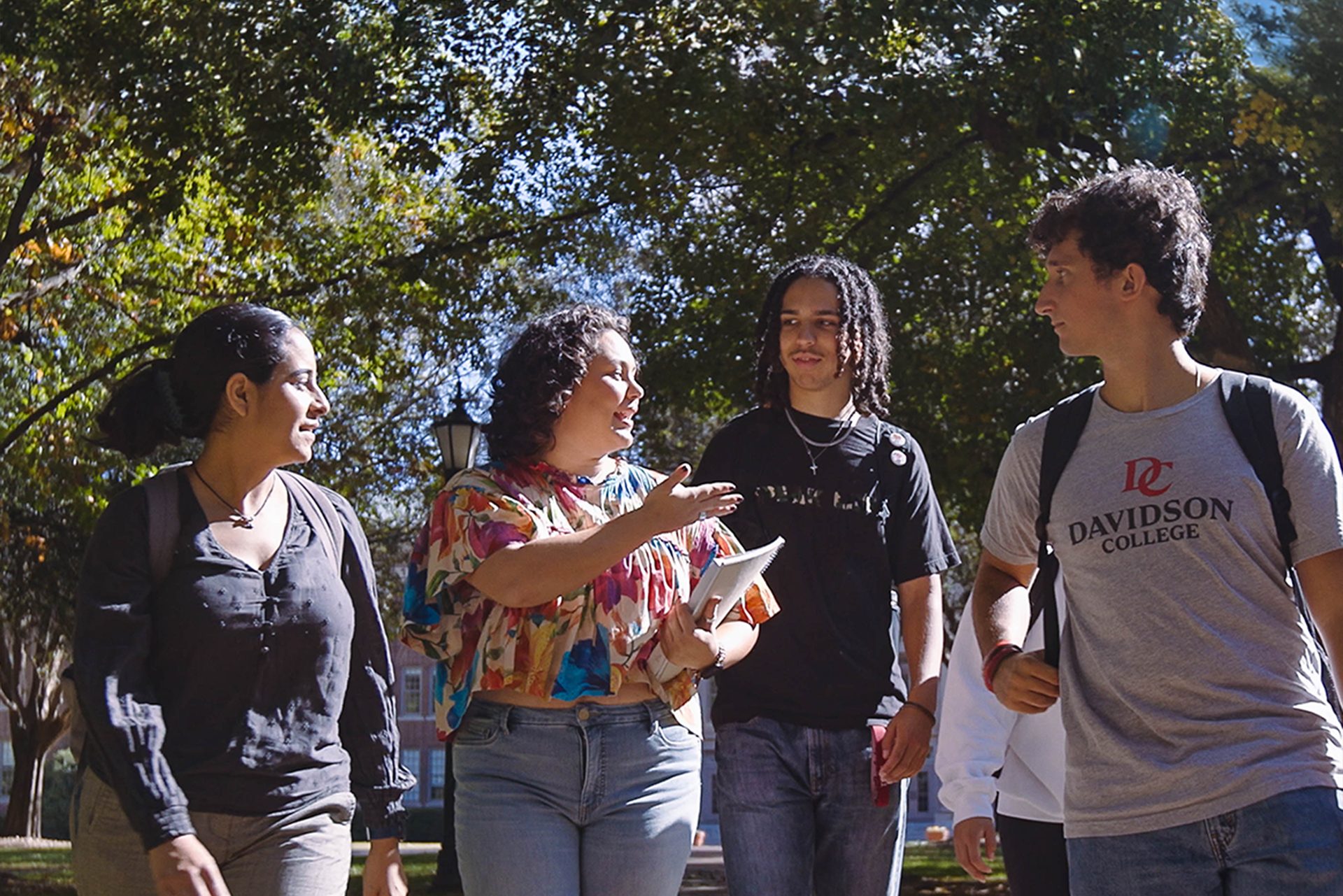 Four students with backpacks and school supplies chat as they walk through campus.