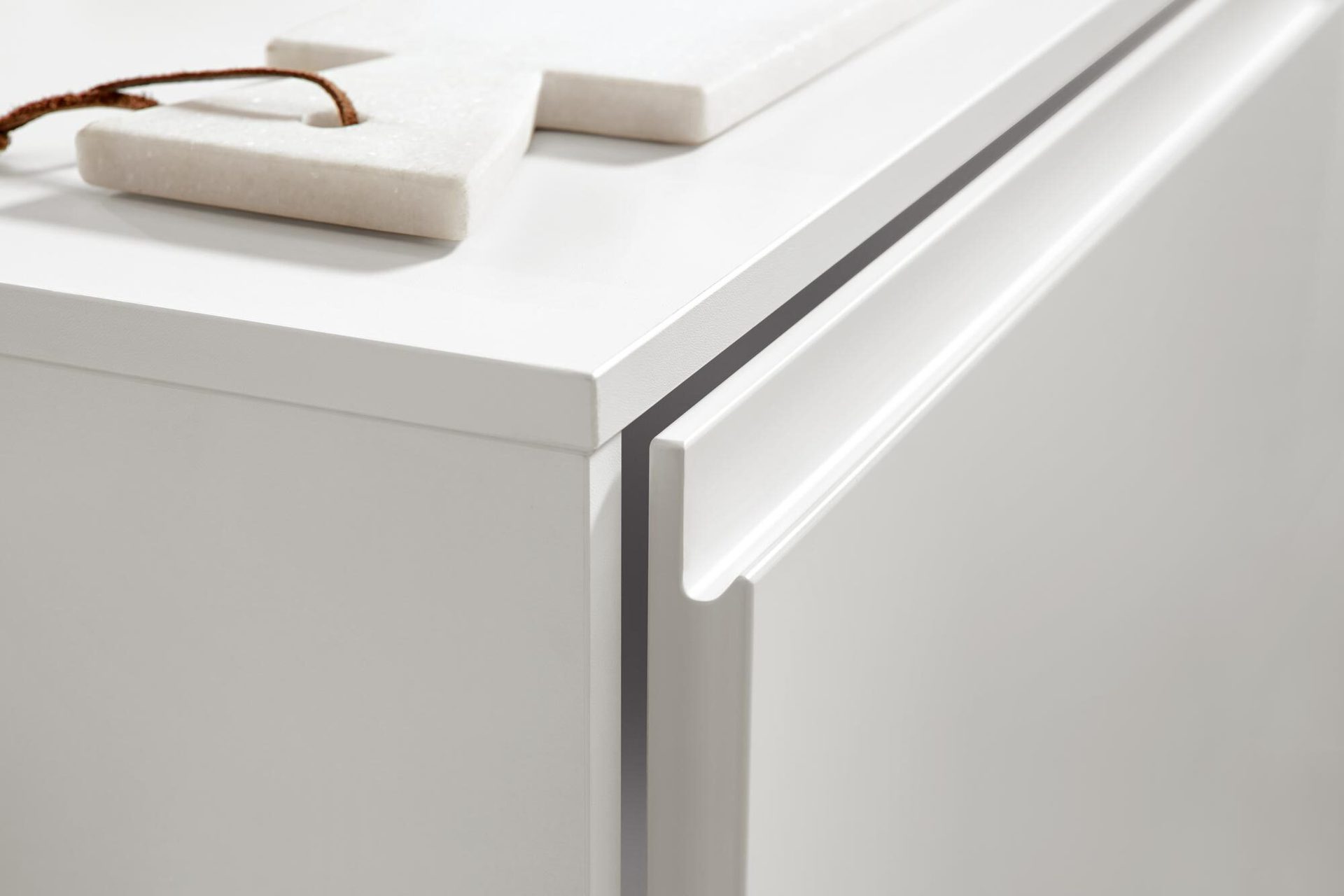 White cabinet with recessed handle and stone decoration on top.