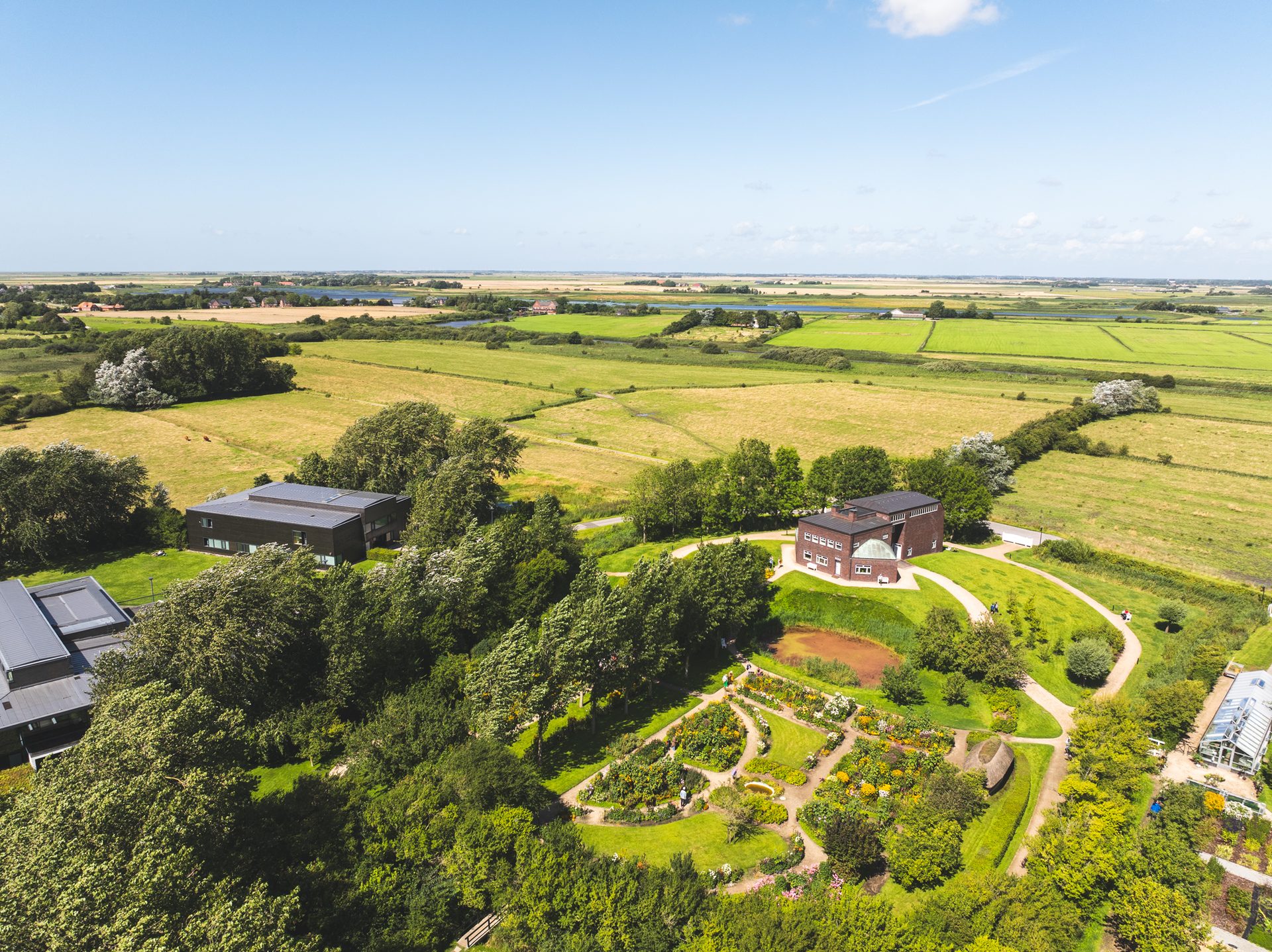 Aerial view of buildings, a botanical garden, and green fields under a blue sky.