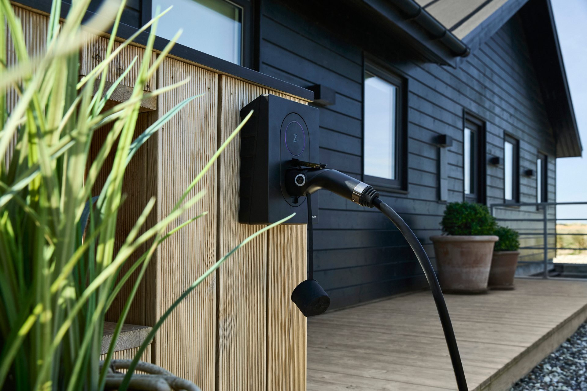 An EV charging station mounted on the side of a modern black and wood-paneled house.