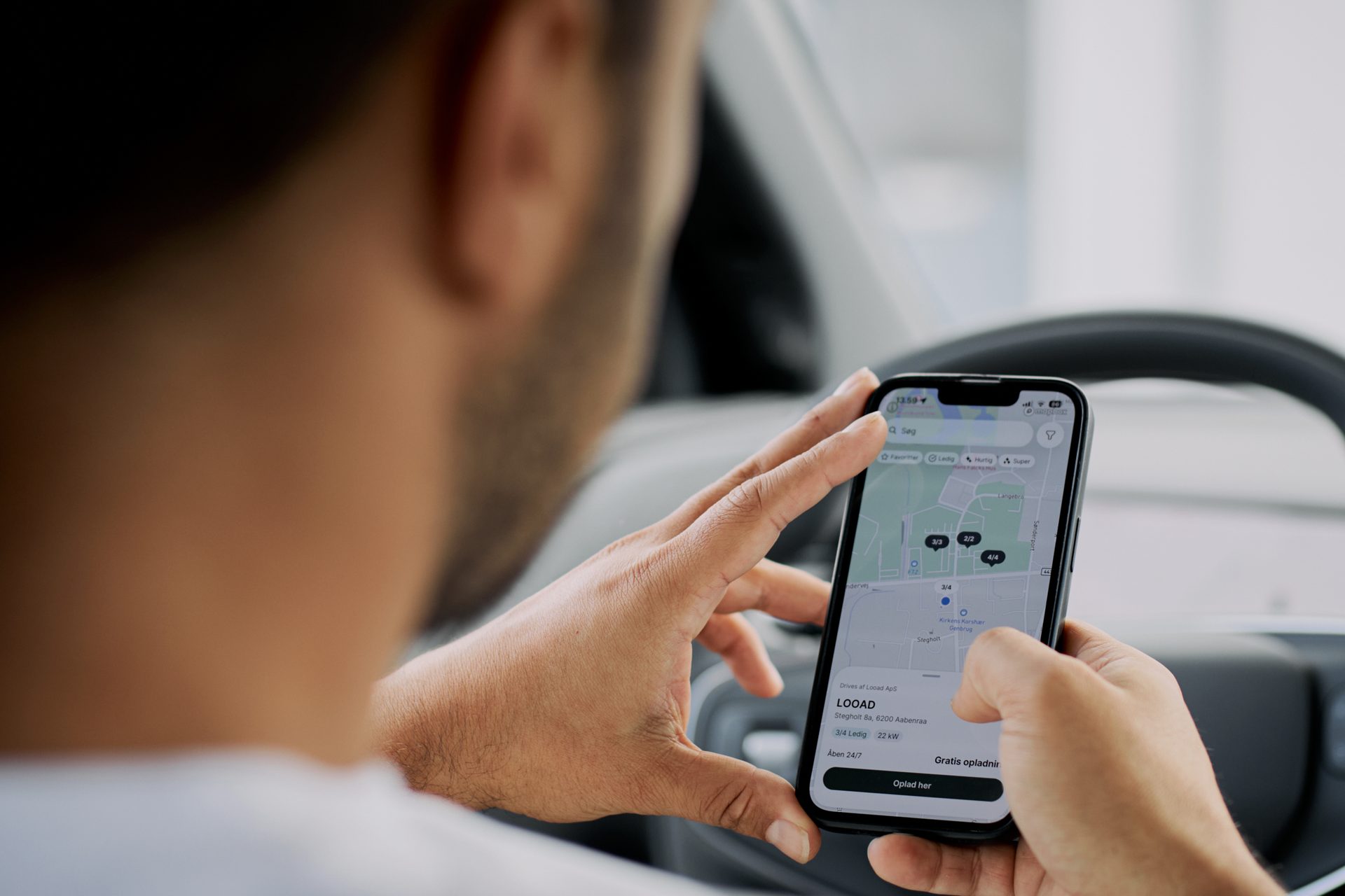 Person using a smartphone map app to find charging stations inside a car.