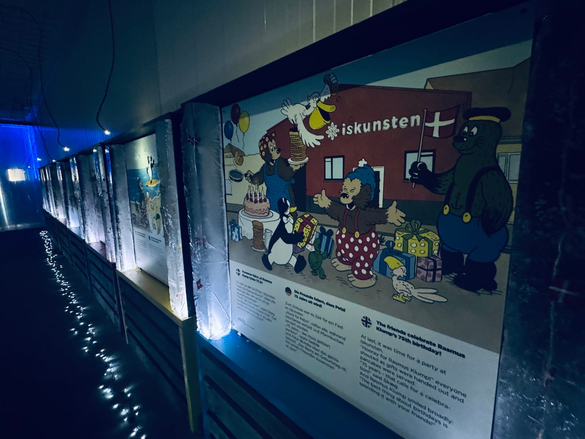 Illuminated hallway with a large cartoon display celebrating Rasmus Klump's 75th birthday with various characters.