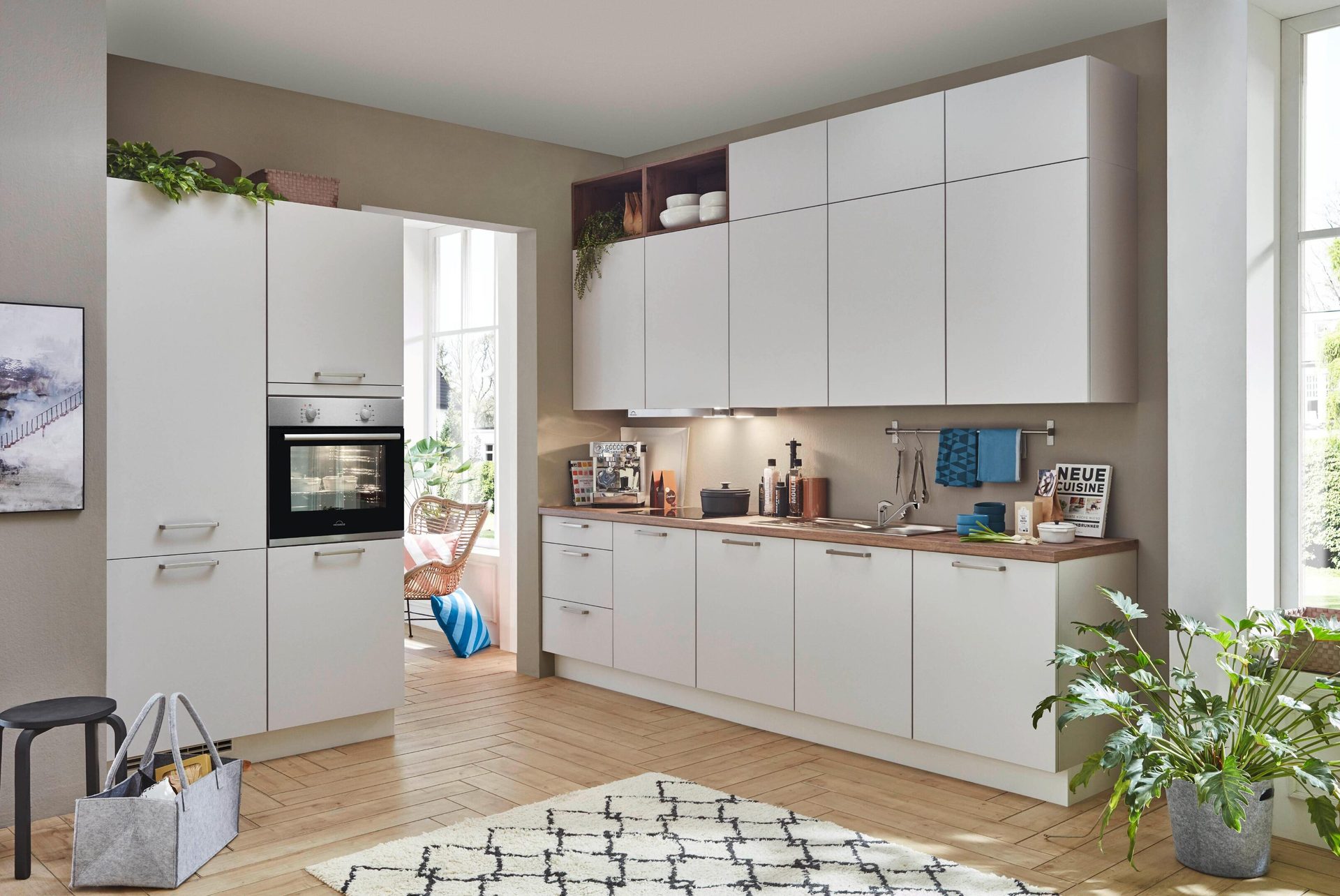 Modern kitchen with white cabinets, wood countertop, built-in oven, large window, and plants.