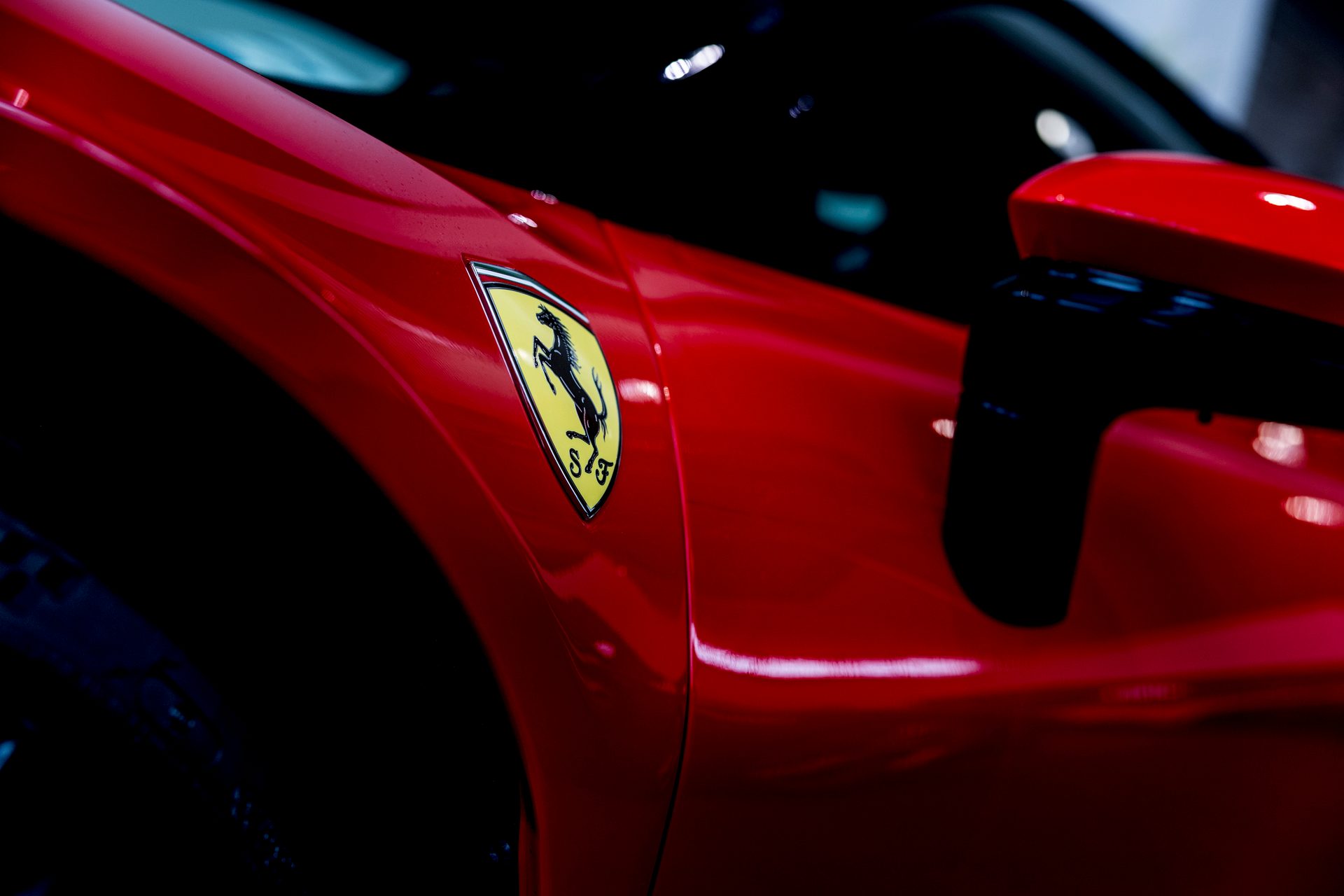 Close-up of a red Ferrari's side, showing the iconic yellow shield emblem and part of the side mirror.