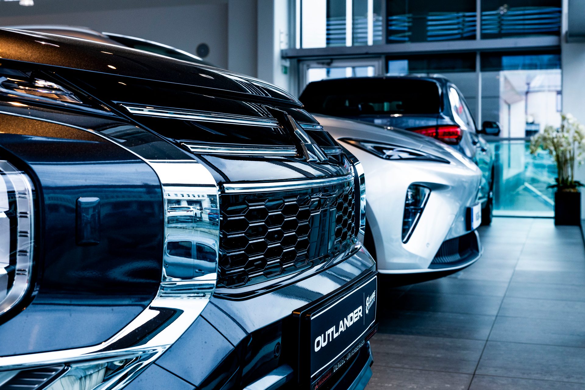Front view of two modern SUVs, a dark one in the foreground and a white one behind, in a car showroom.
