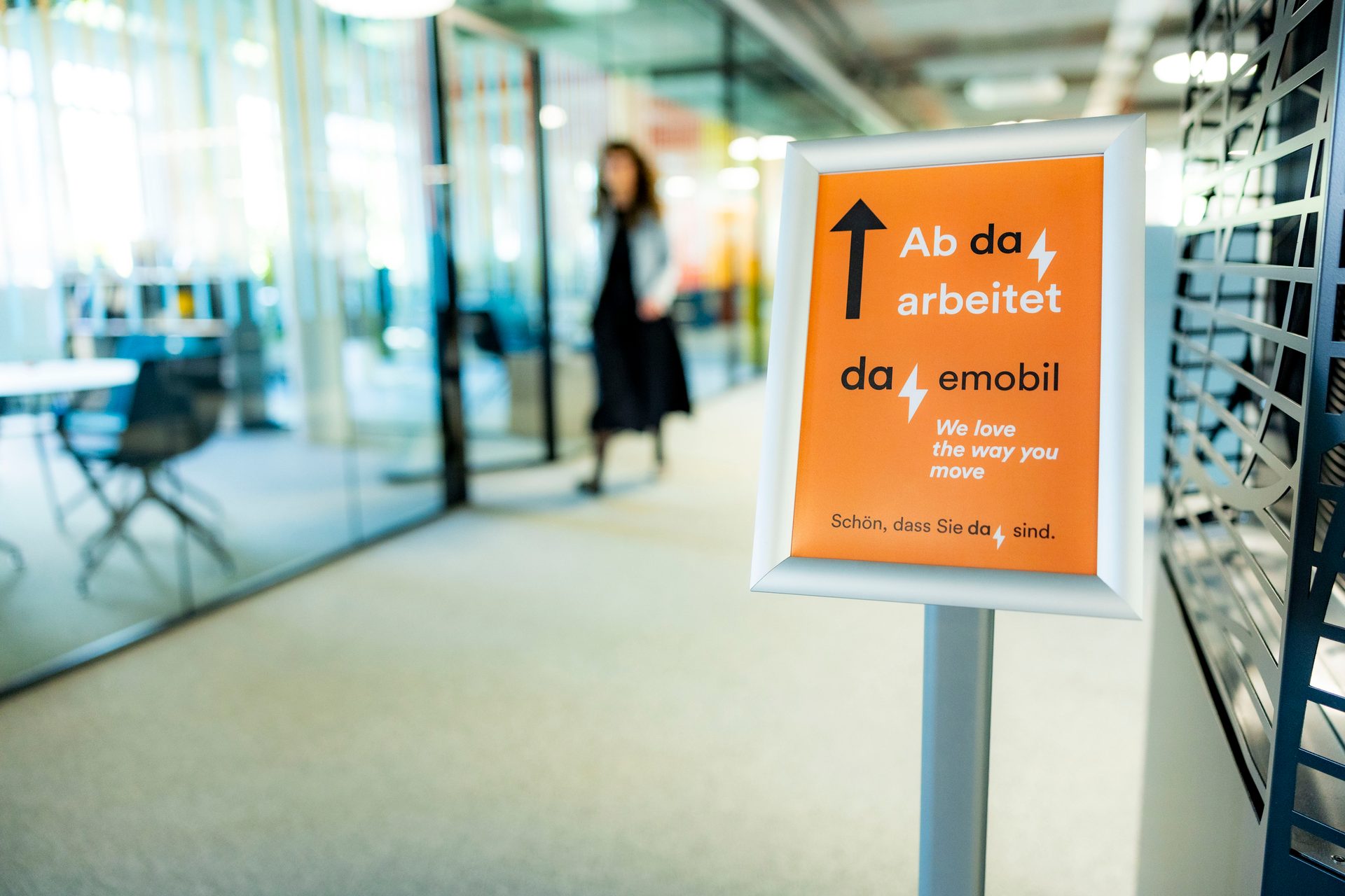 Modern office hallway with a sign reading 'Ab da arbeitet da emobil' and 'We love the way you move'.