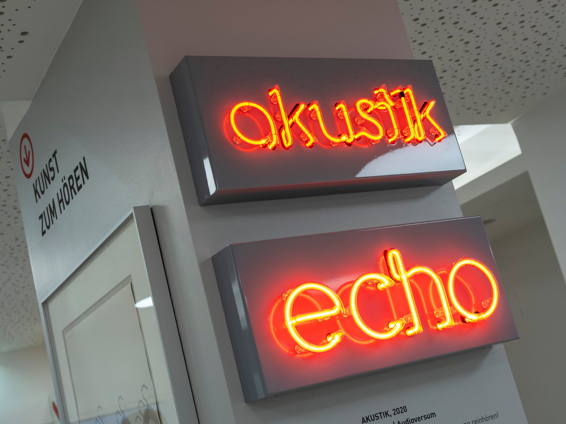 Two glowing red neon signs, "Okustik" and "echo", displayed on a grey wall with German text.