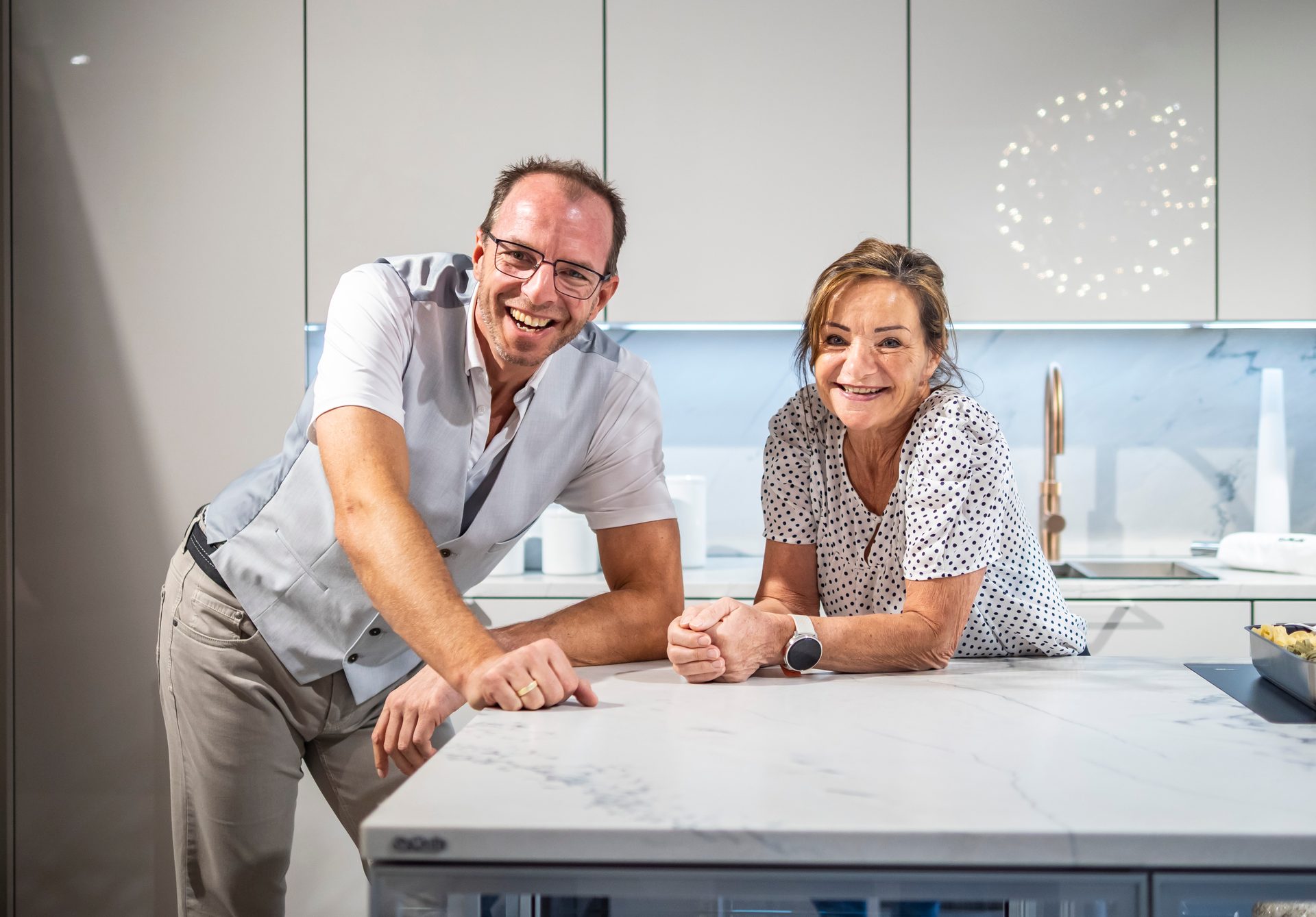 Smiling man and woman lean on a kitchen counter in a modern kitchen.