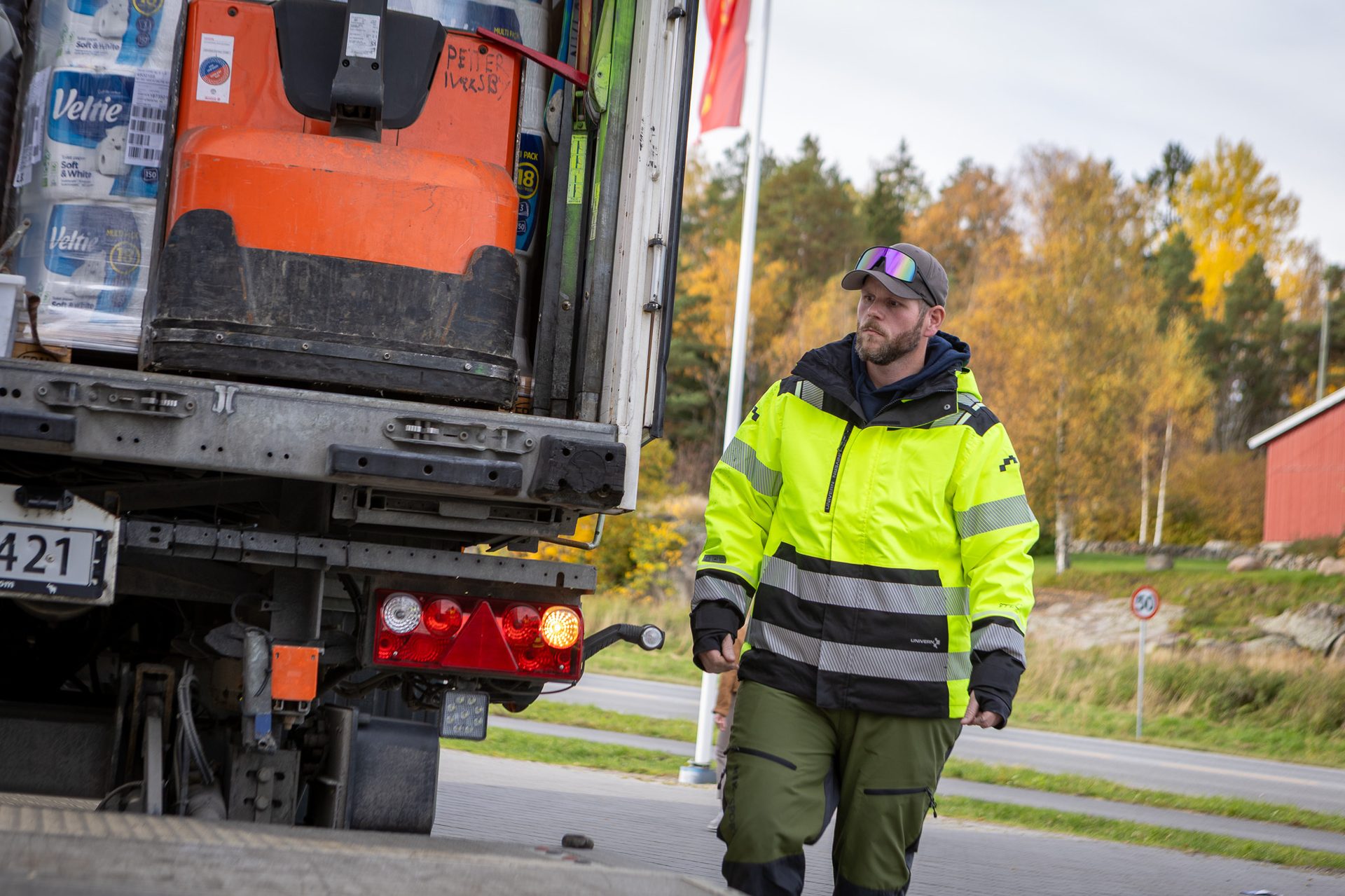 Man in hi-vis jacket walks near truck unloading toilet paper with a pallet jack.
