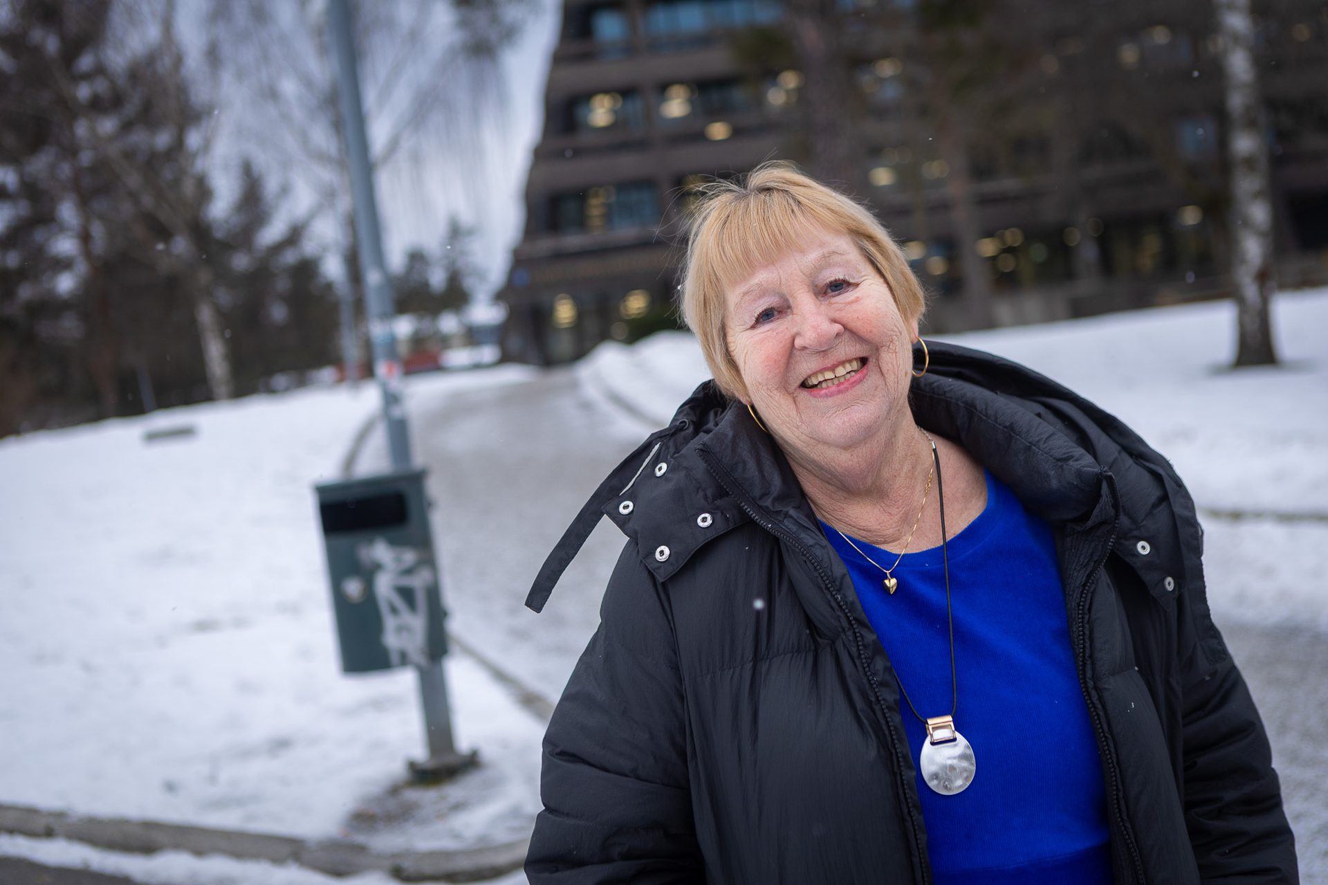 A smiling older woman in a black jacket outdoors on a snowy day.