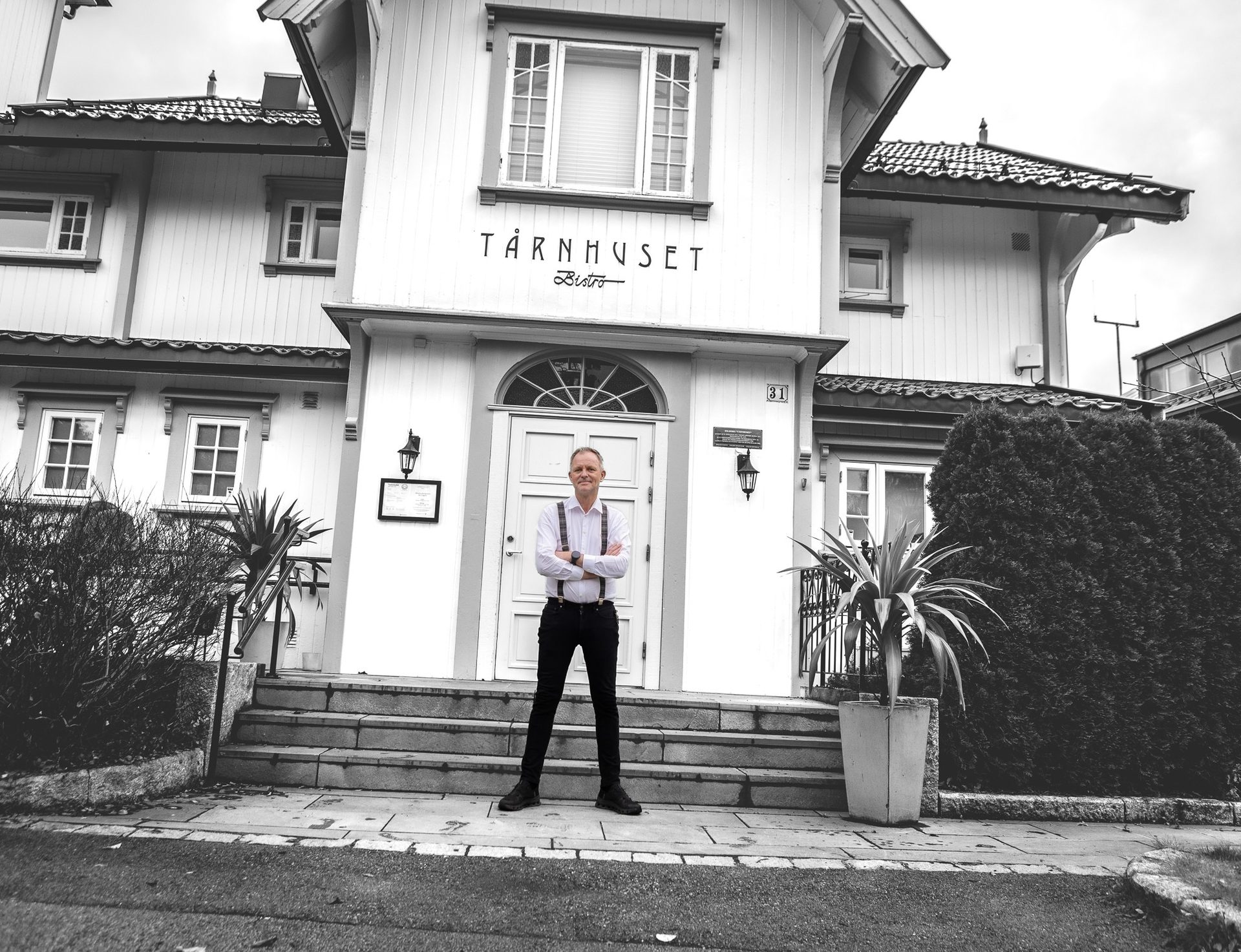 Black and white photo of a man in suspenders in front of TÅRNHUSET Bistro.
